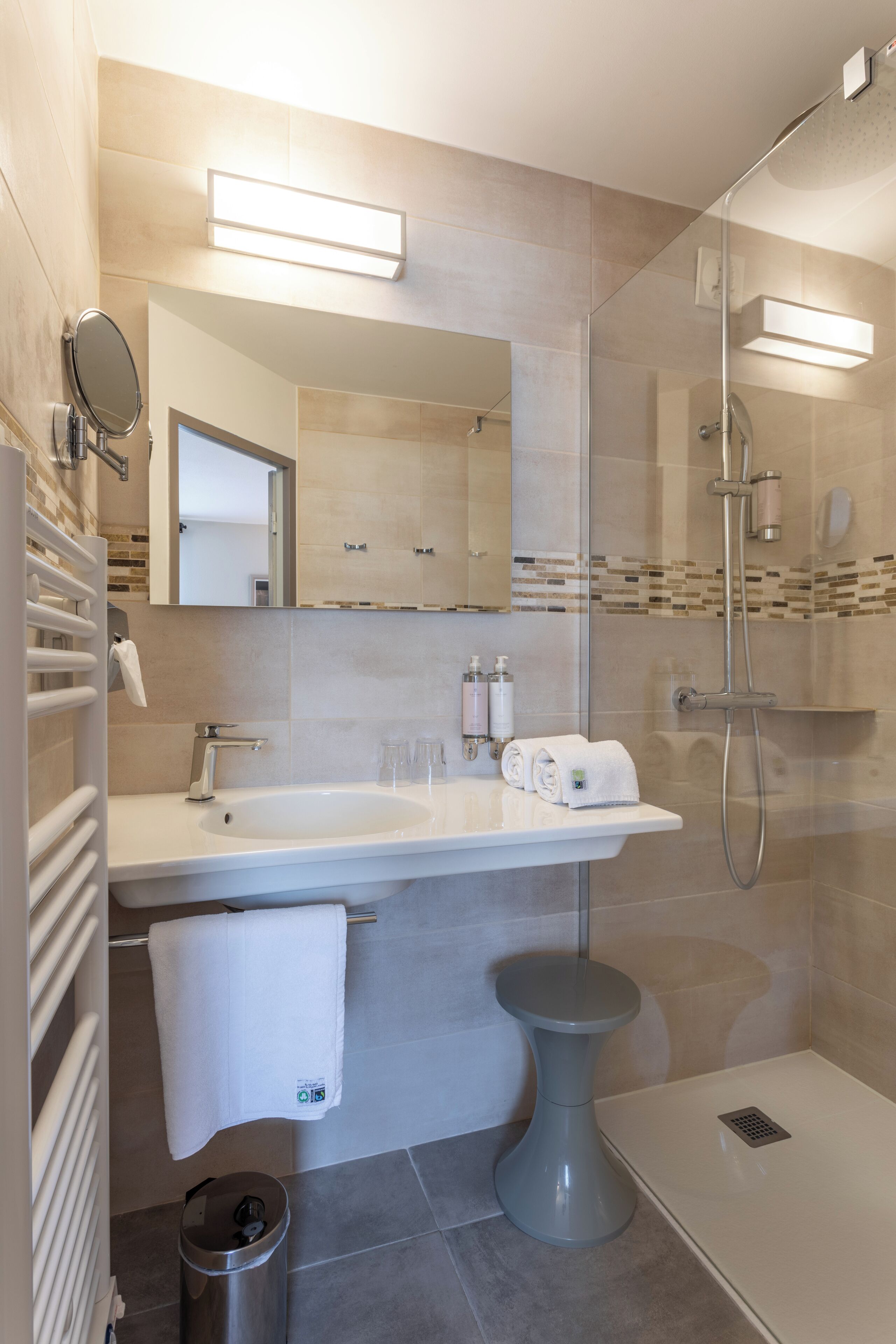 Une salle de bain moderne avec une douche à parois de verre, un lavabo blanc avec un miroir et un petit tabouret.
