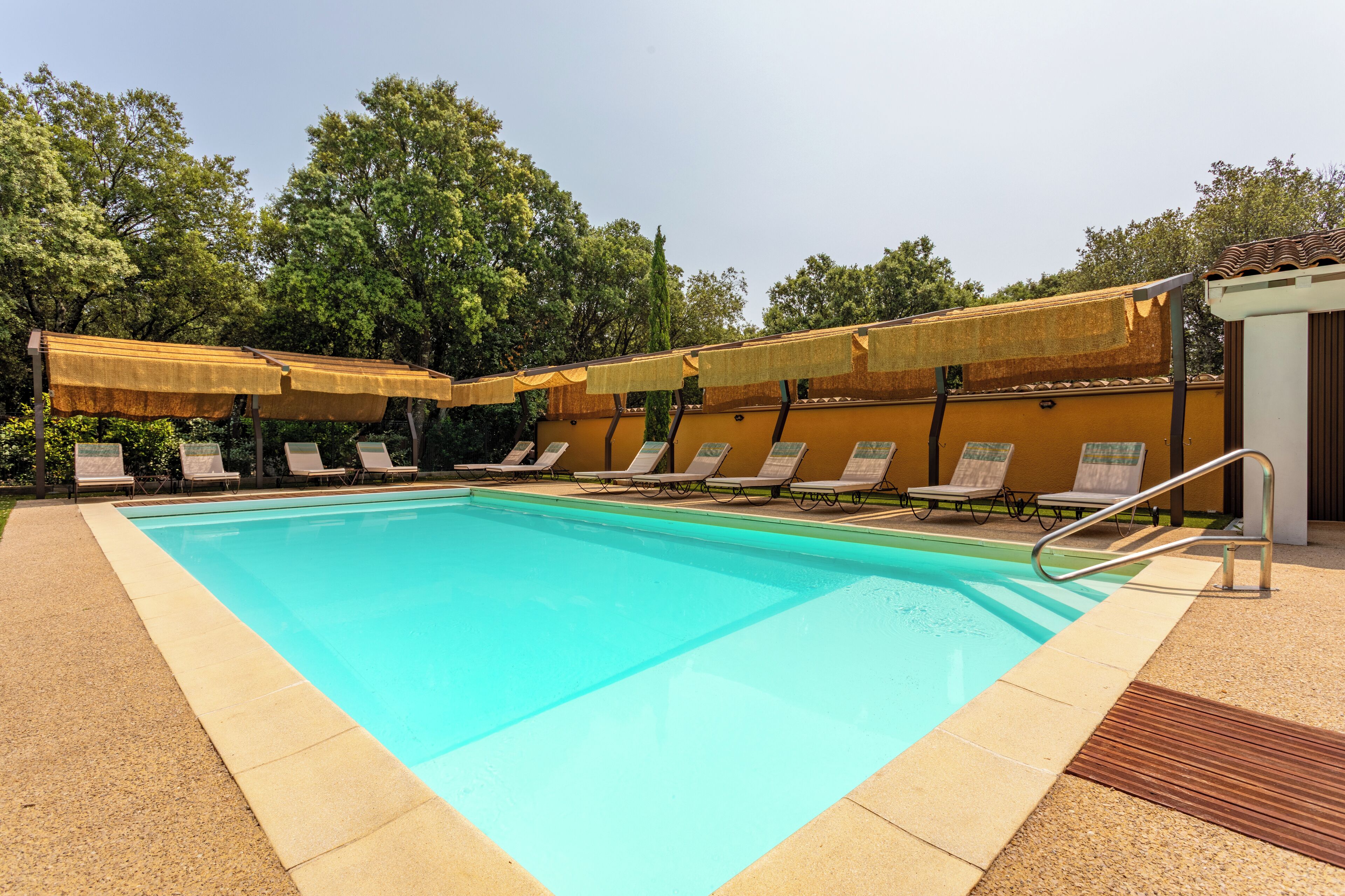 A swimming pool with lounge chairs and umbrellas, surrounded by trees.