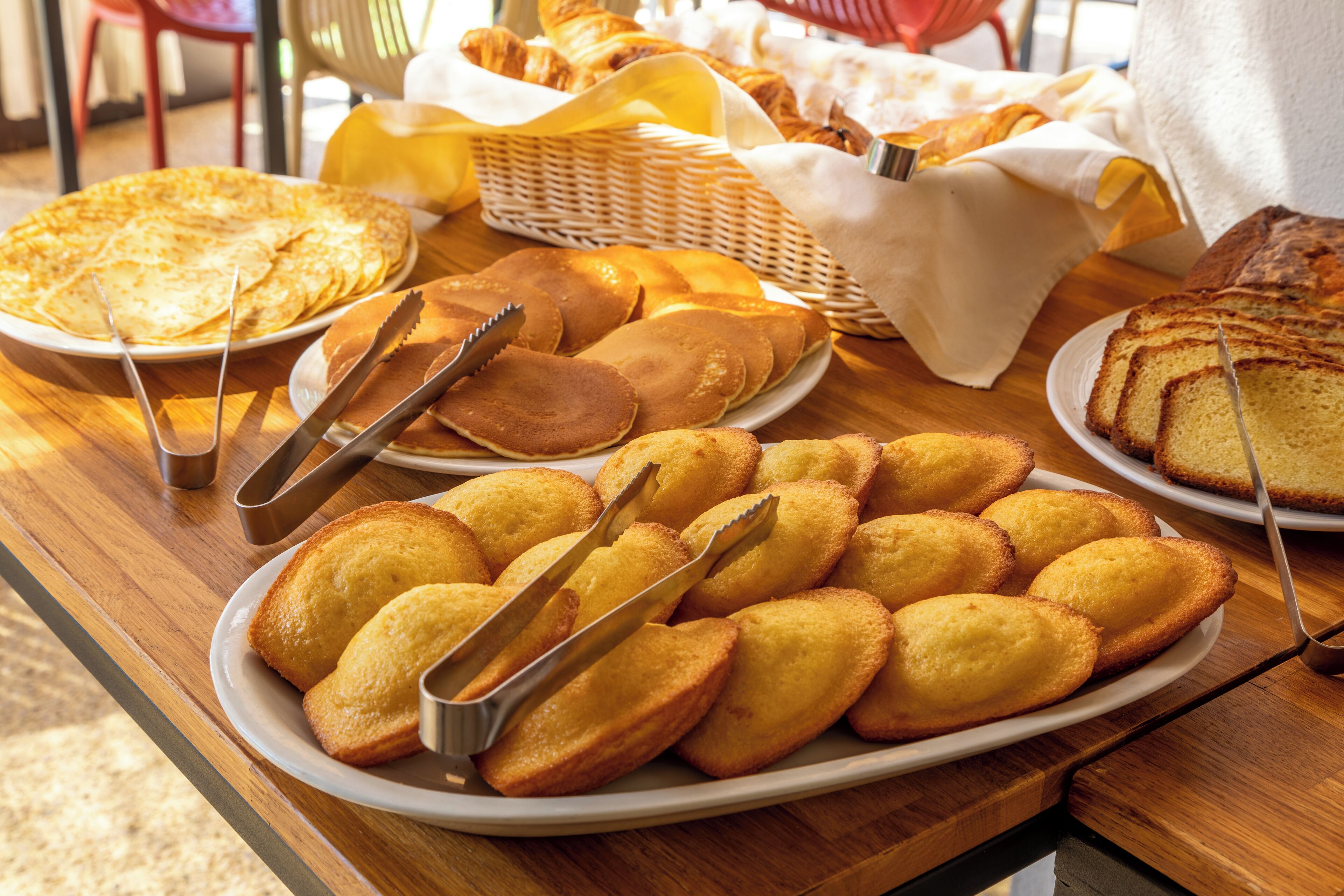 A breakfast buffet with various pastries and bread on white plates, arranged on a wooden table.