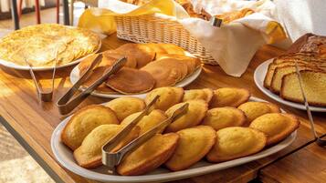 A breakfast buffet with various pastries and bread on white plates, arranged on a wooden table.