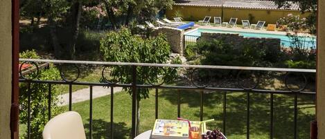 A balcony with two beige chairs and a small table with a menu and drinks. A pool and greenery are visible in the background.