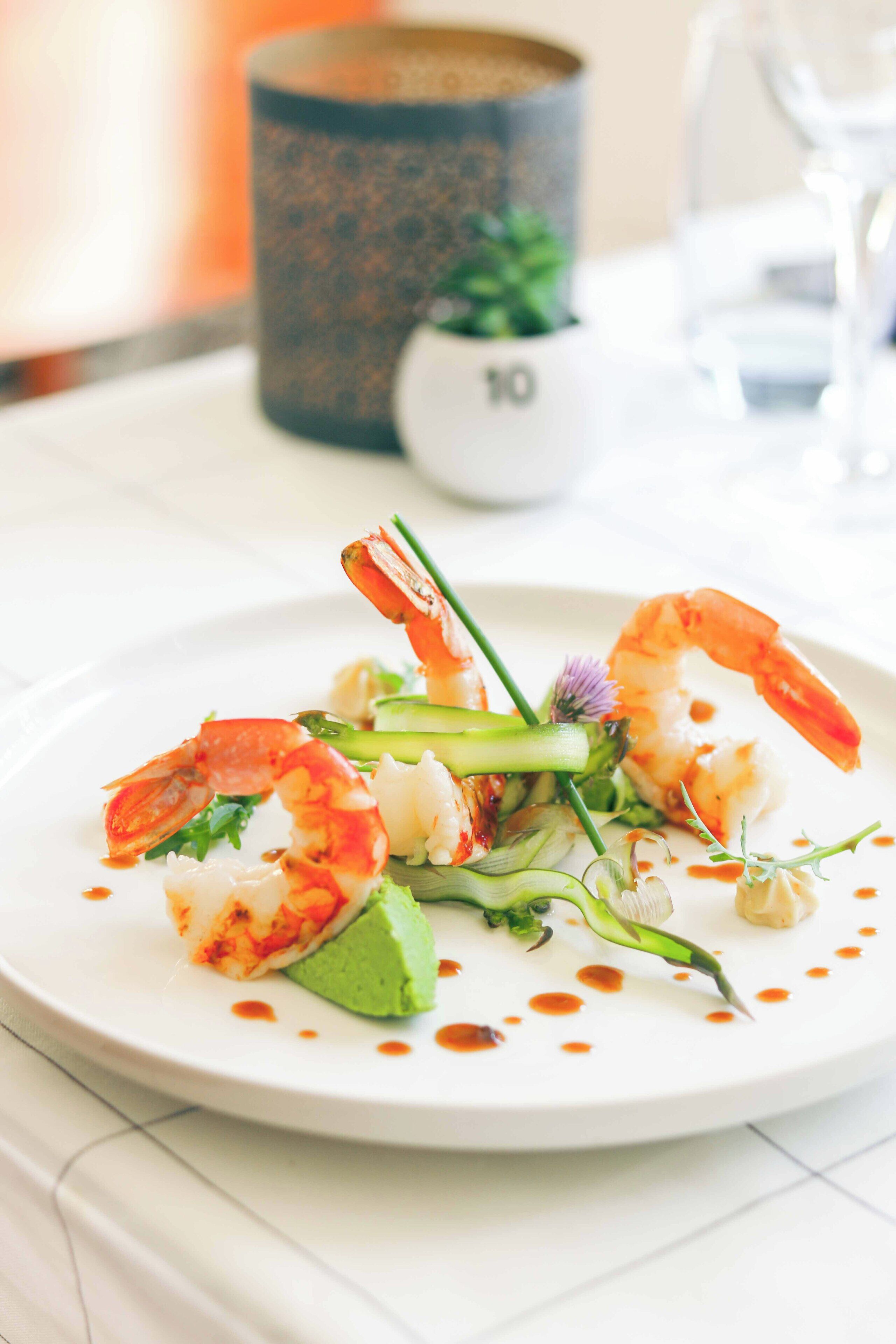 A plate of food with shrimp, avocado, and greens on a white plate.
