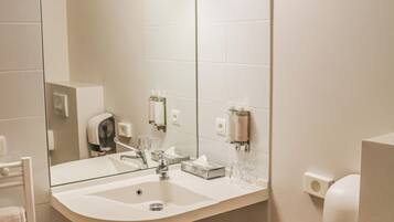 Une salle de bain avec un lavabo sur colonne, un grand miroir et un sèche-mains.