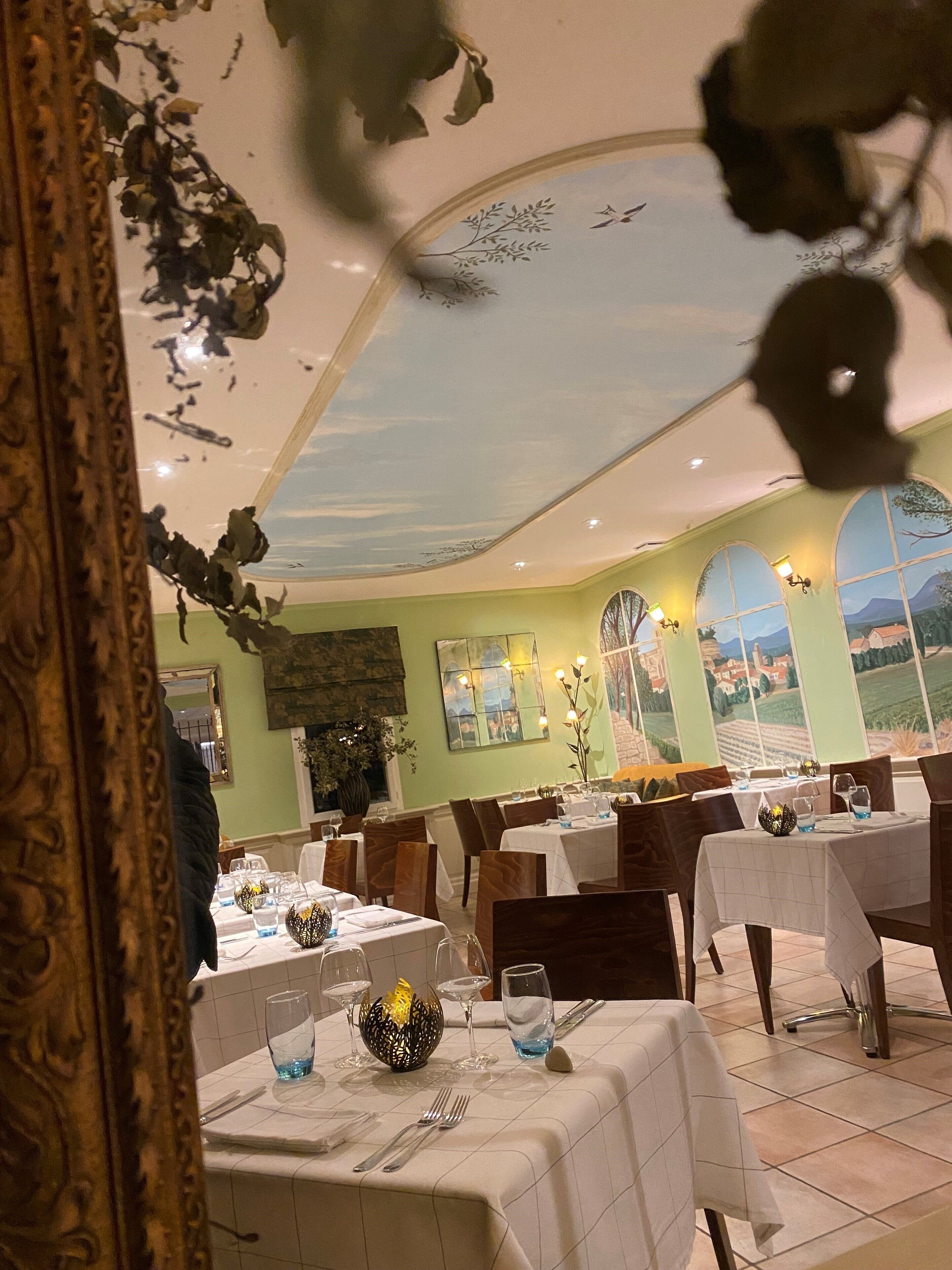 A restaurant with tables set for dining, a mural on the wall, and a view of the countryside through large windows.