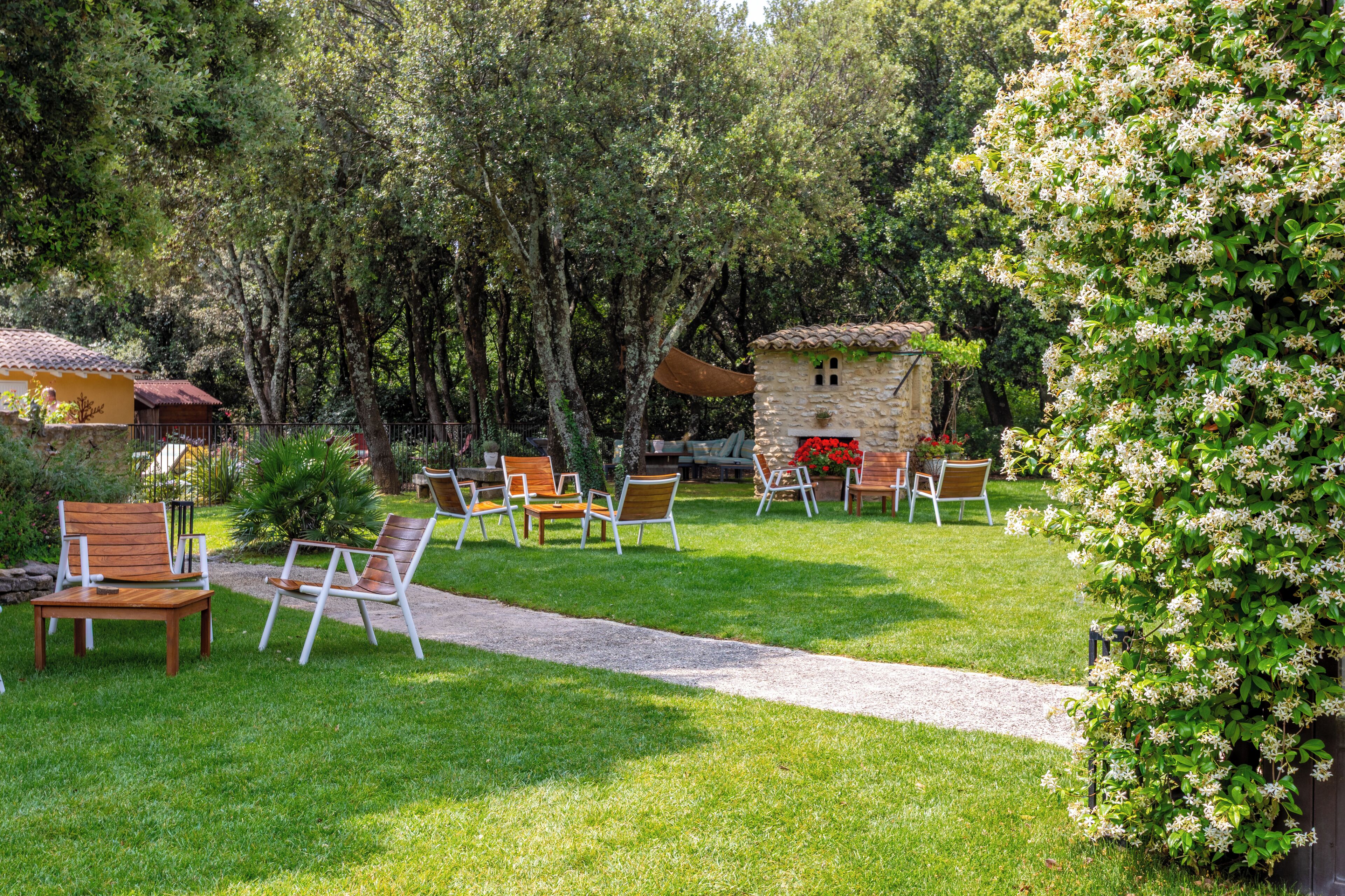 Un jardín con mobiliario exterior, estructuras de piedra y abundante vegetación.