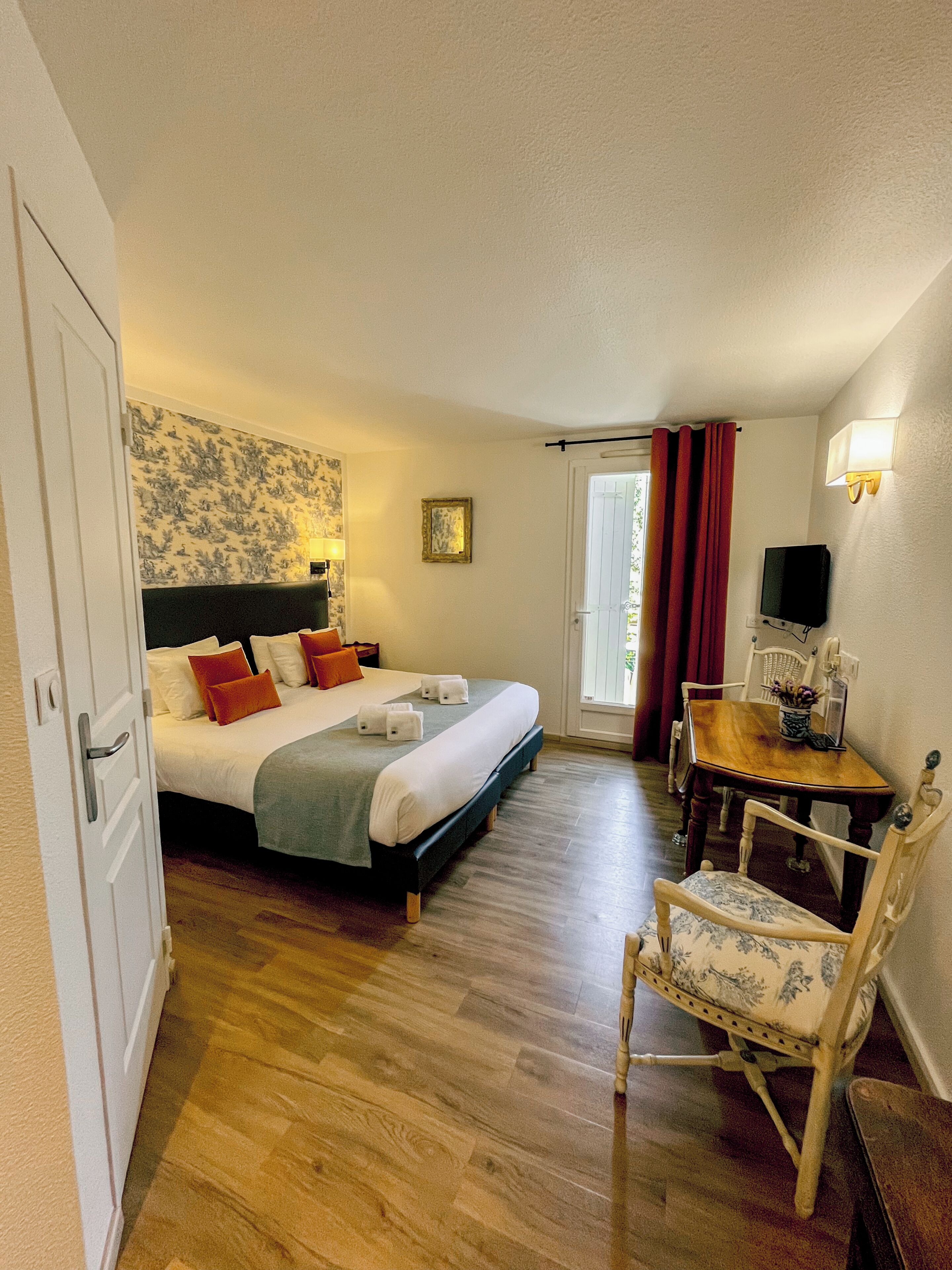 A hotel room with a bed, a desk, a chair, a TV, and a door.