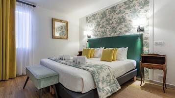 Ein ordentlich eingerichtetes Hotelzimmer mit einem Bett, Nachttischen, einer Bank, einem Spiegel und einer Wand mit Blumenmuster-Tapete.
