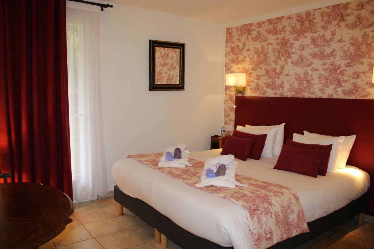 A hotel room with a large bed, a wooden nightstand, a red curtain, and a framed picture on the wall.