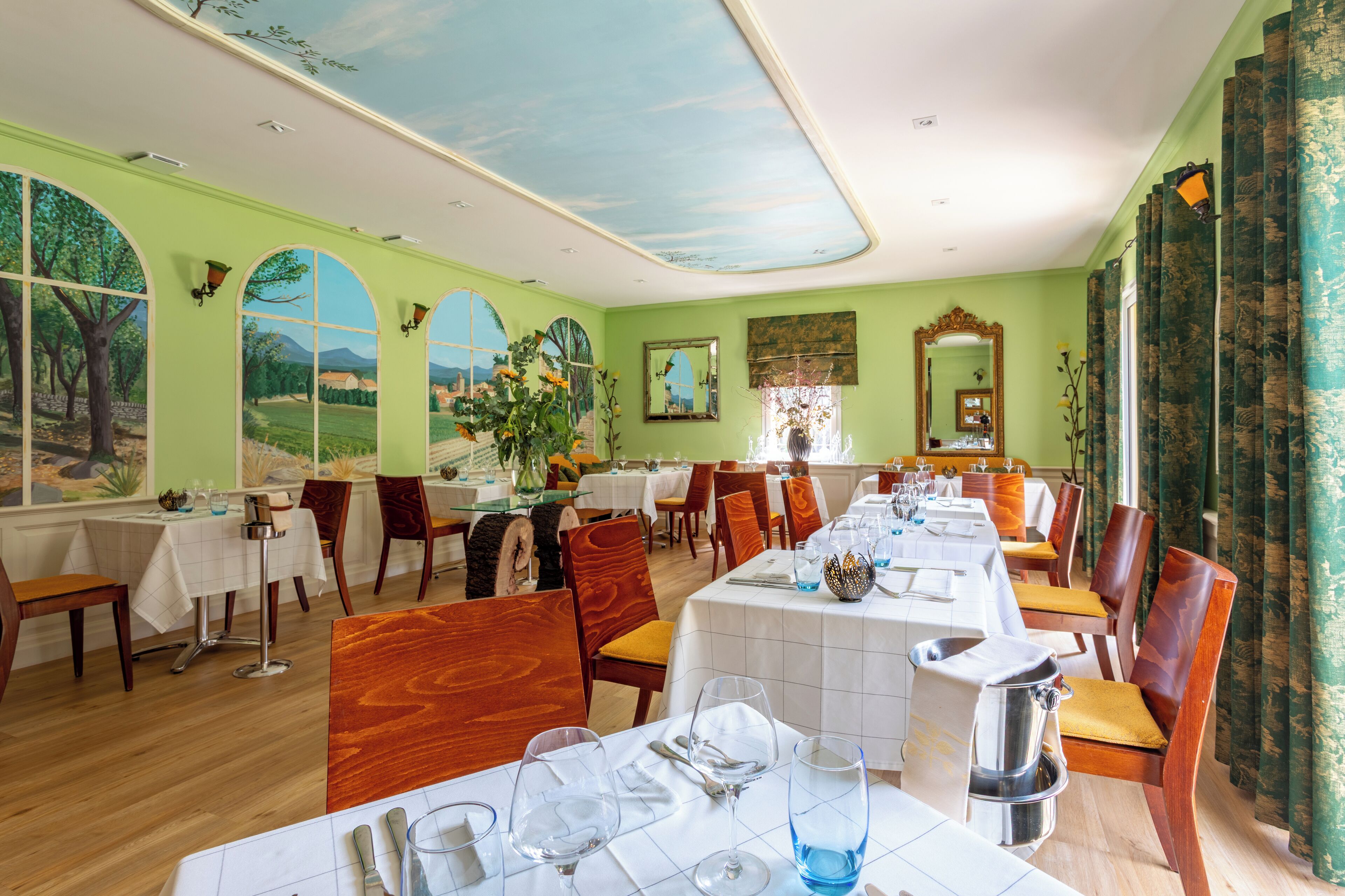 Ein Restaurant mit mehreren Tischen und Stühlen, einer Wandmalerei und einer Decke mit gemaltem Himmel.
