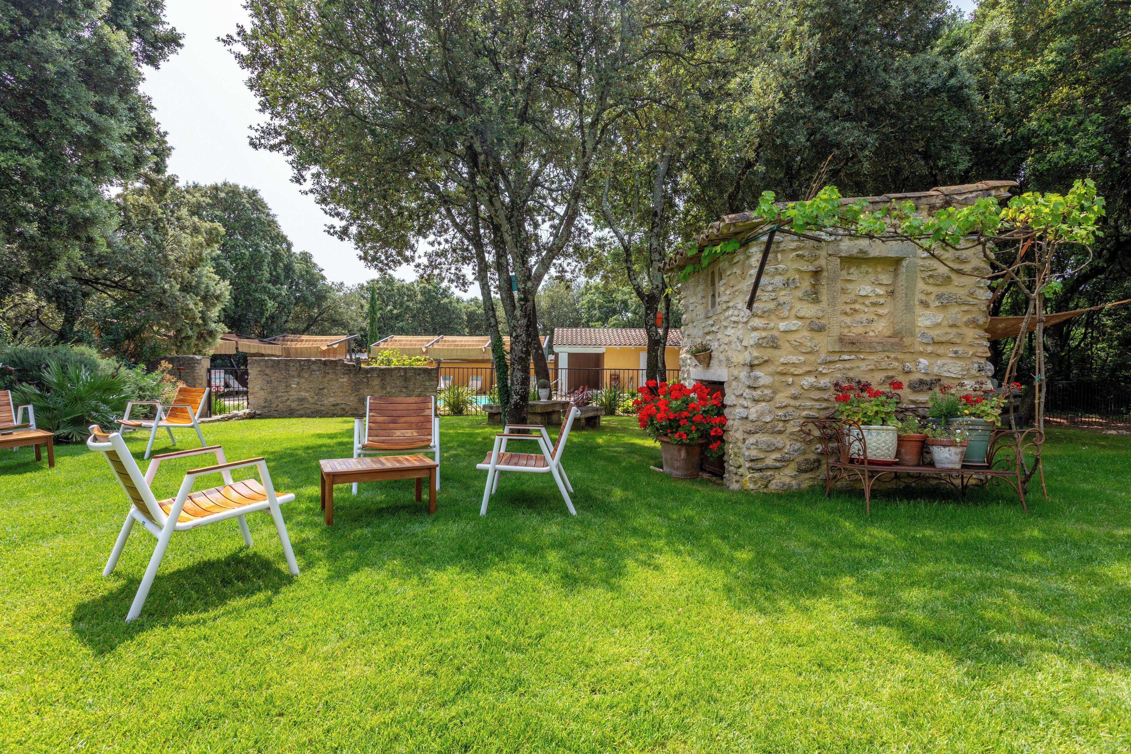 A stone building with a wooden bench and chairs in a lush garden.