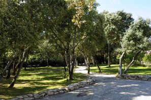 A gravel path bordered by a stone wall, surrounded by lush green trees and grass. - Logis Hôtel La Bastide de Grignan & Restaurant La Chênaie (Grignan)