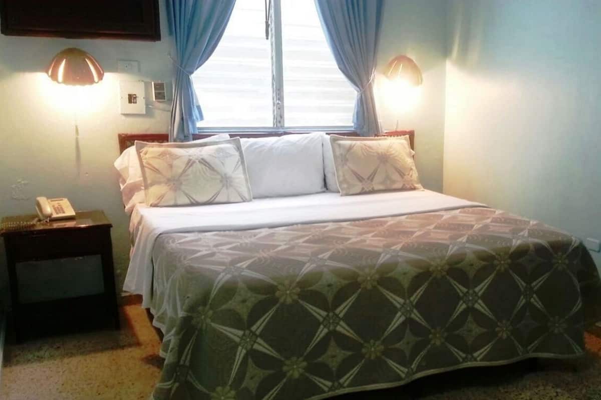 A bedroom with a bed, two bedside lamps, a nightstand, a desk, and a mirror.