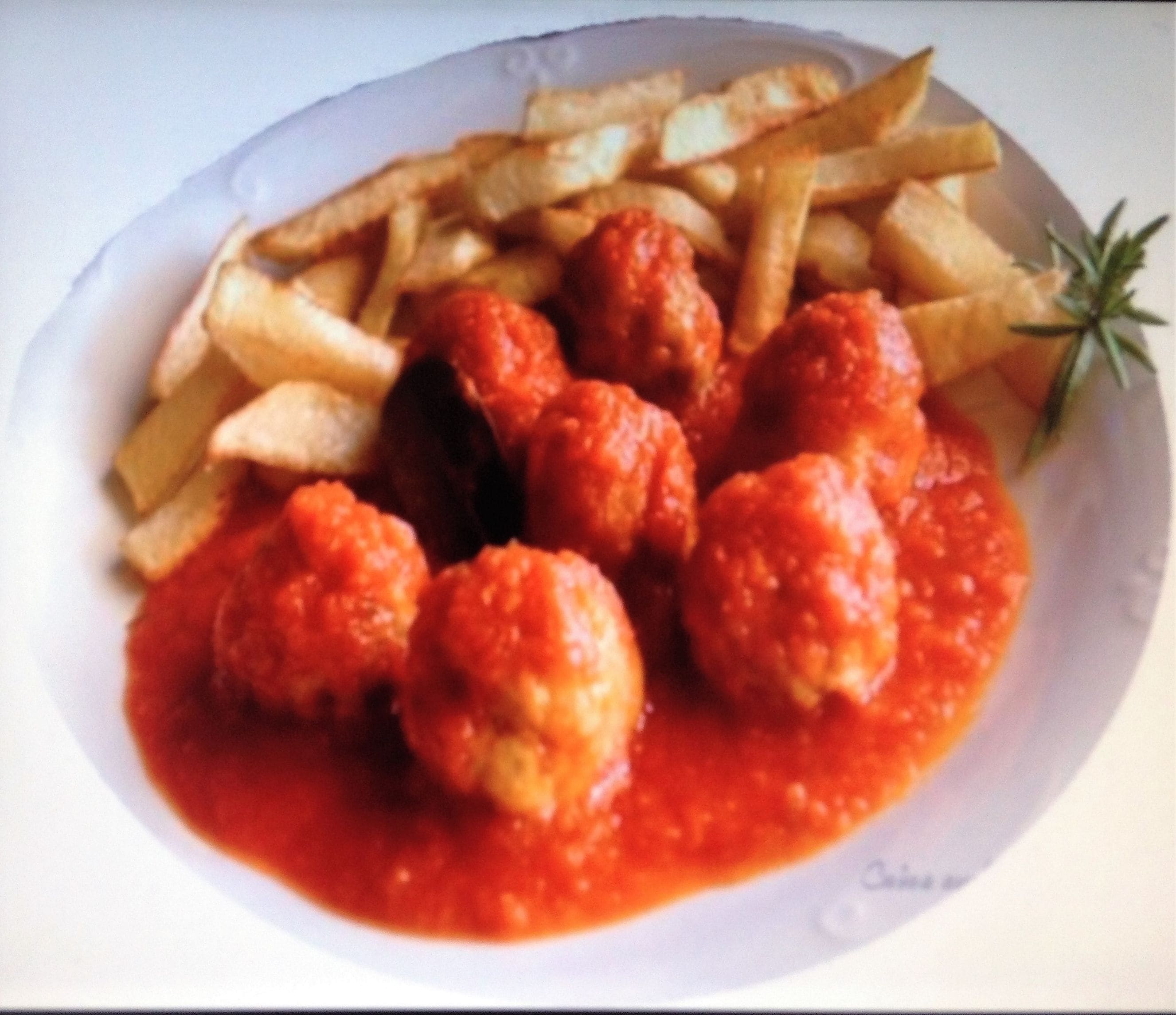 Un plato de albóndigas en salsa de tomate con papas fritas.