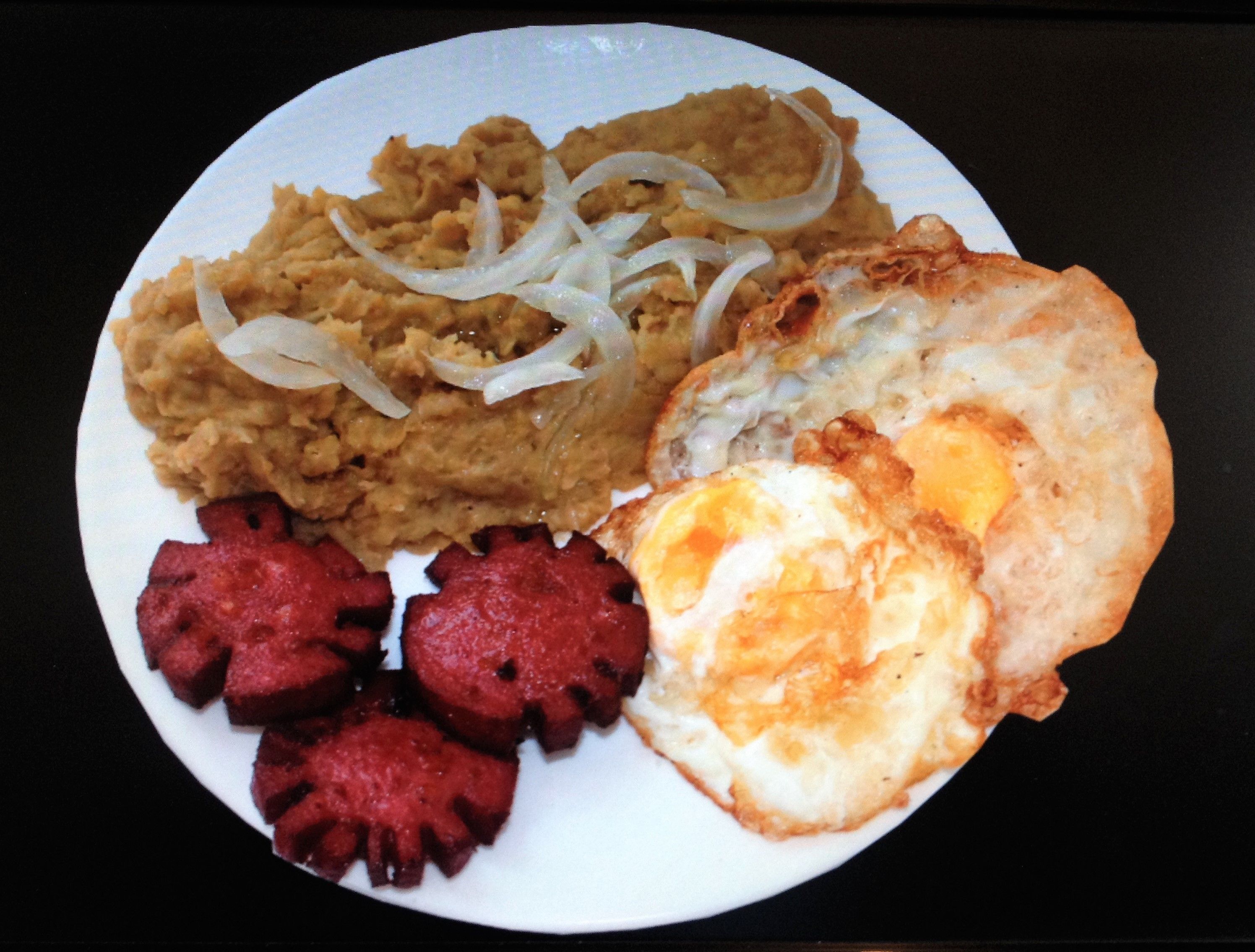 A plate with a fried egg, a slice of toast, and a portion of beans with onions.