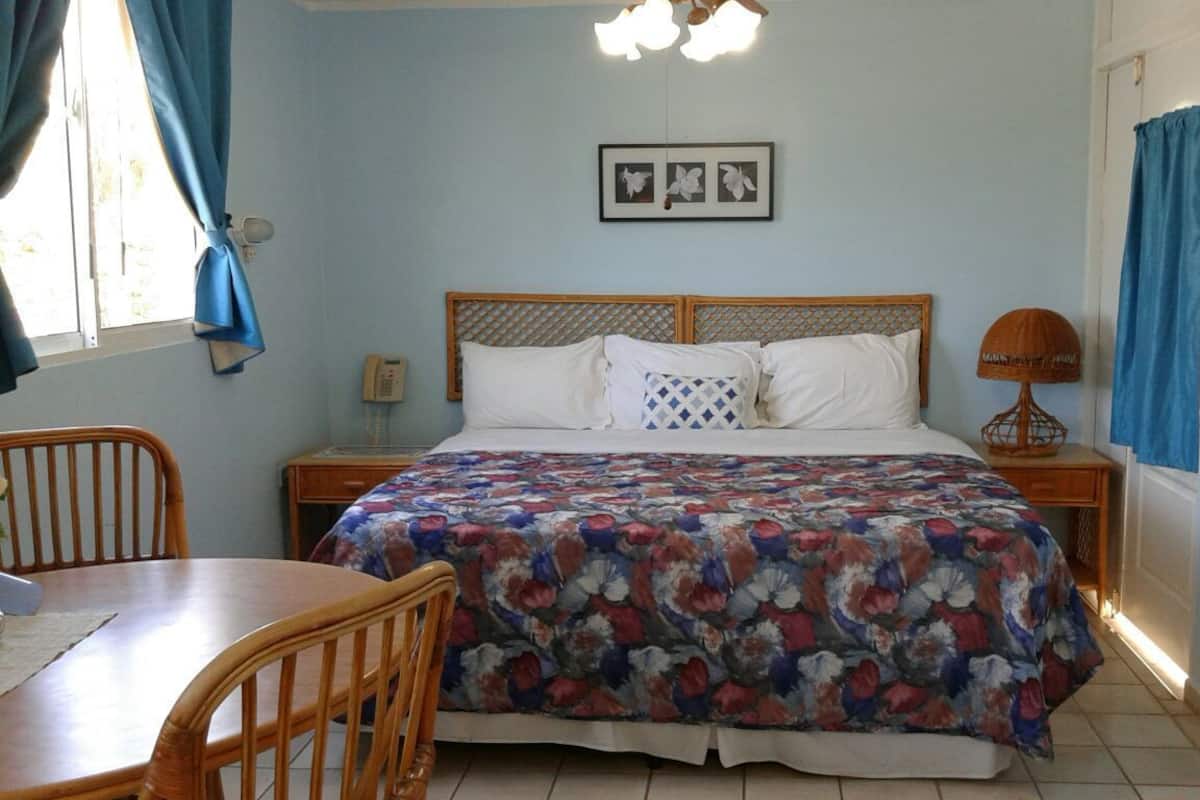 A bedroom with a bed, a wooden headboard, a bedside table with a lamp, a chair, and a window with curtains.