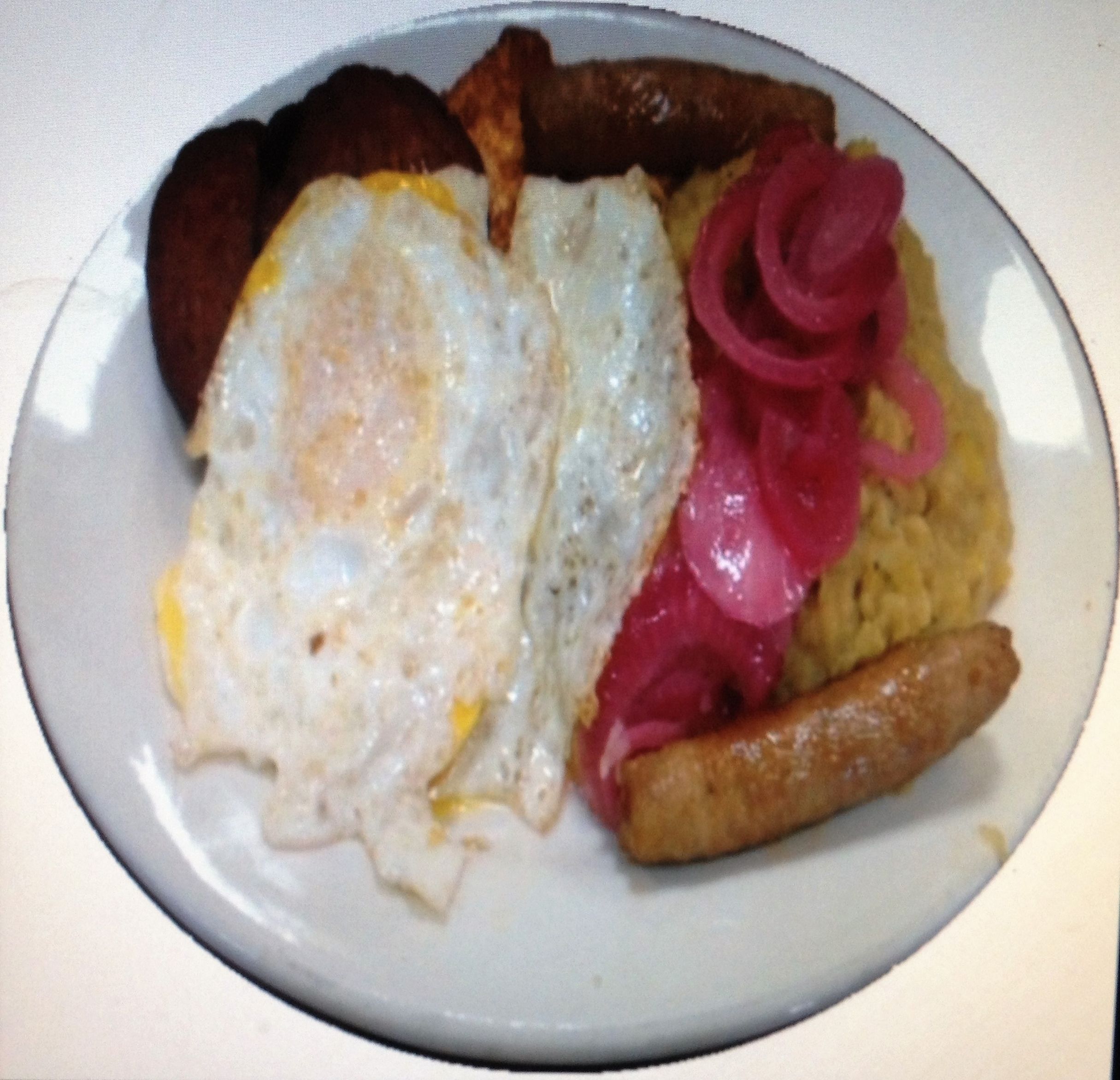 A plate with two fried eggs, a sausage, and pickled vegetables.