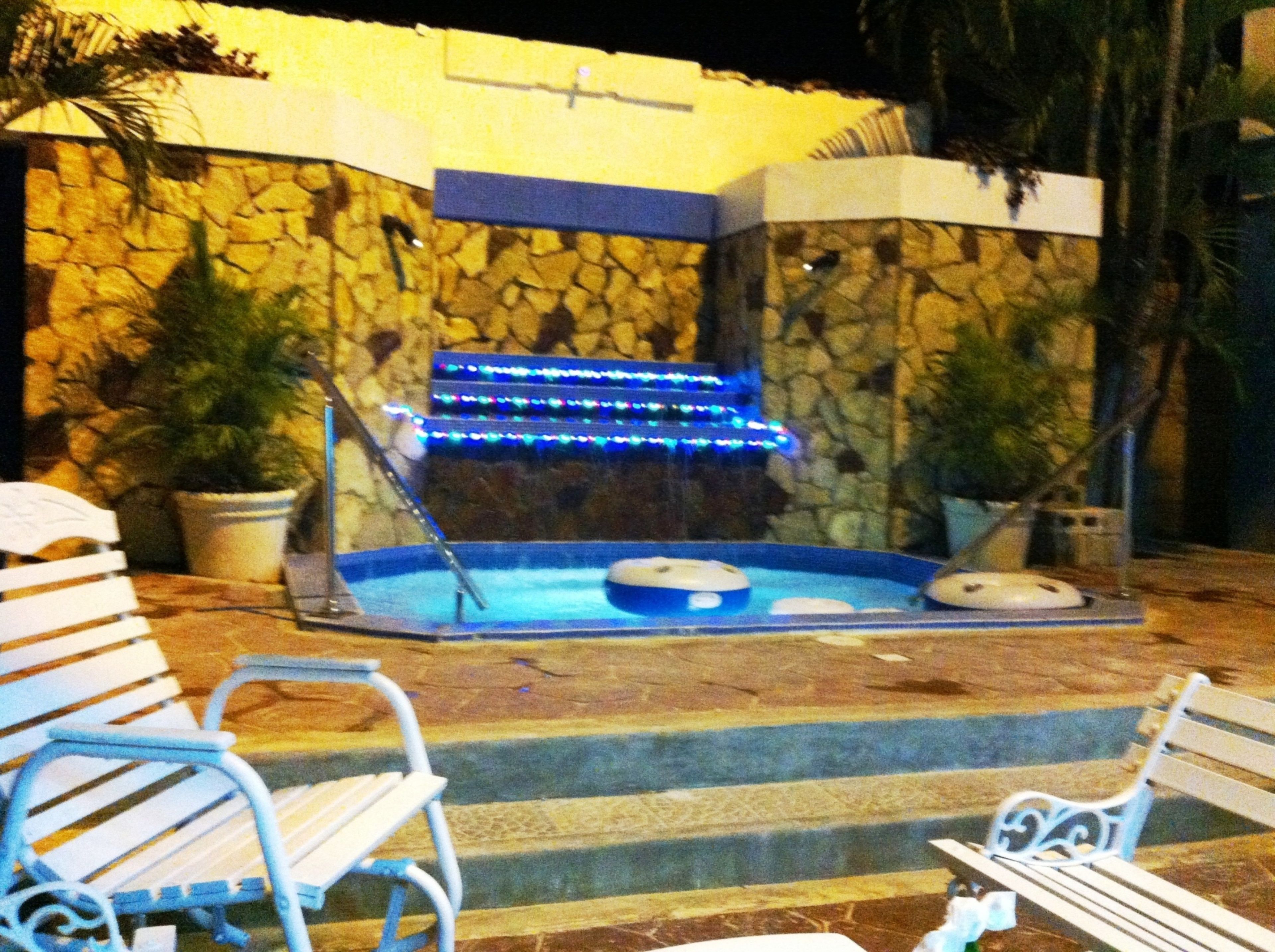 A stone wall with a hot tub and blue LED lights, benches, and potted plants.