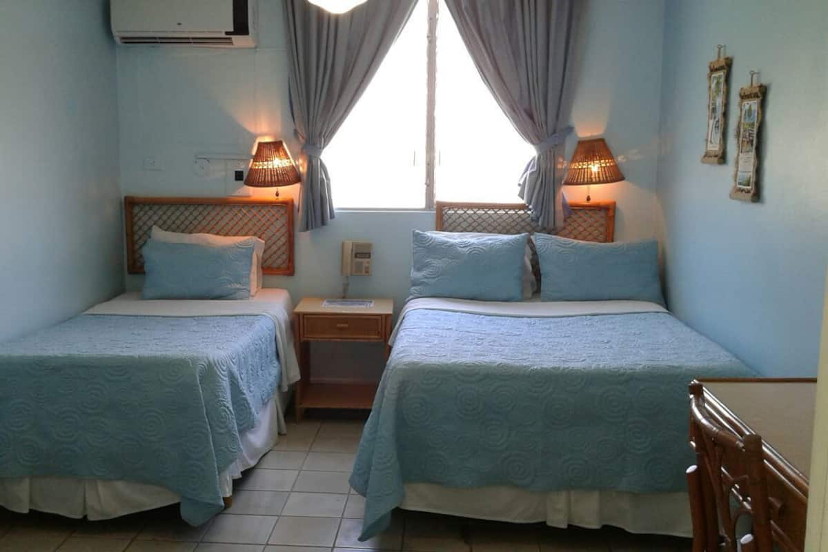 A room with two beds, each with a headboard, a bedside table, and a lamp.