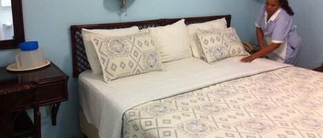 Una cama bien hecha con almohadones estampados y un cabecero de madera en una habitación con paredes azul claro y dos lámparas de pared.