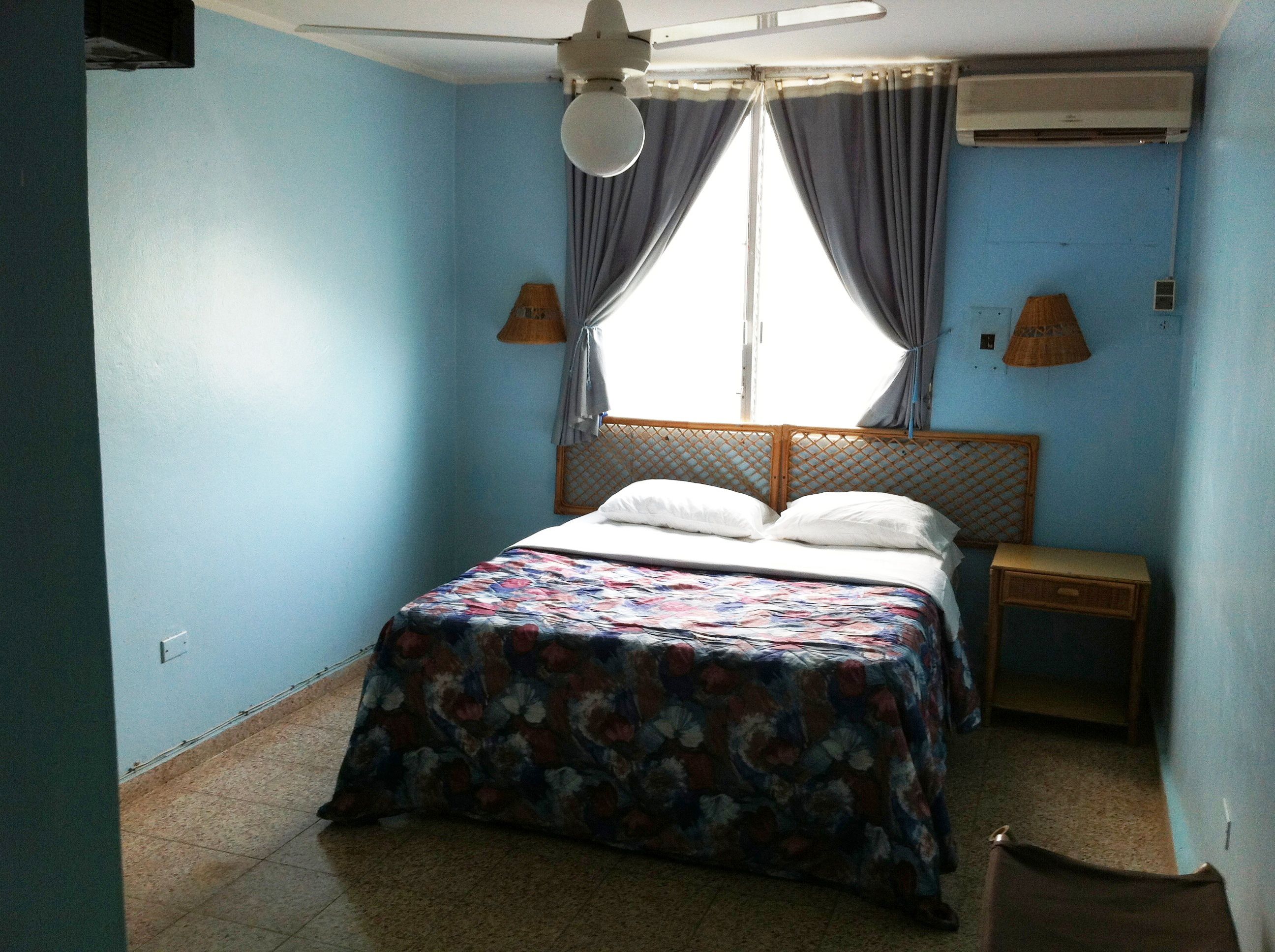 A bedroom with a bed, a nightstand, a ceiling fan, and an air conditioning unit.