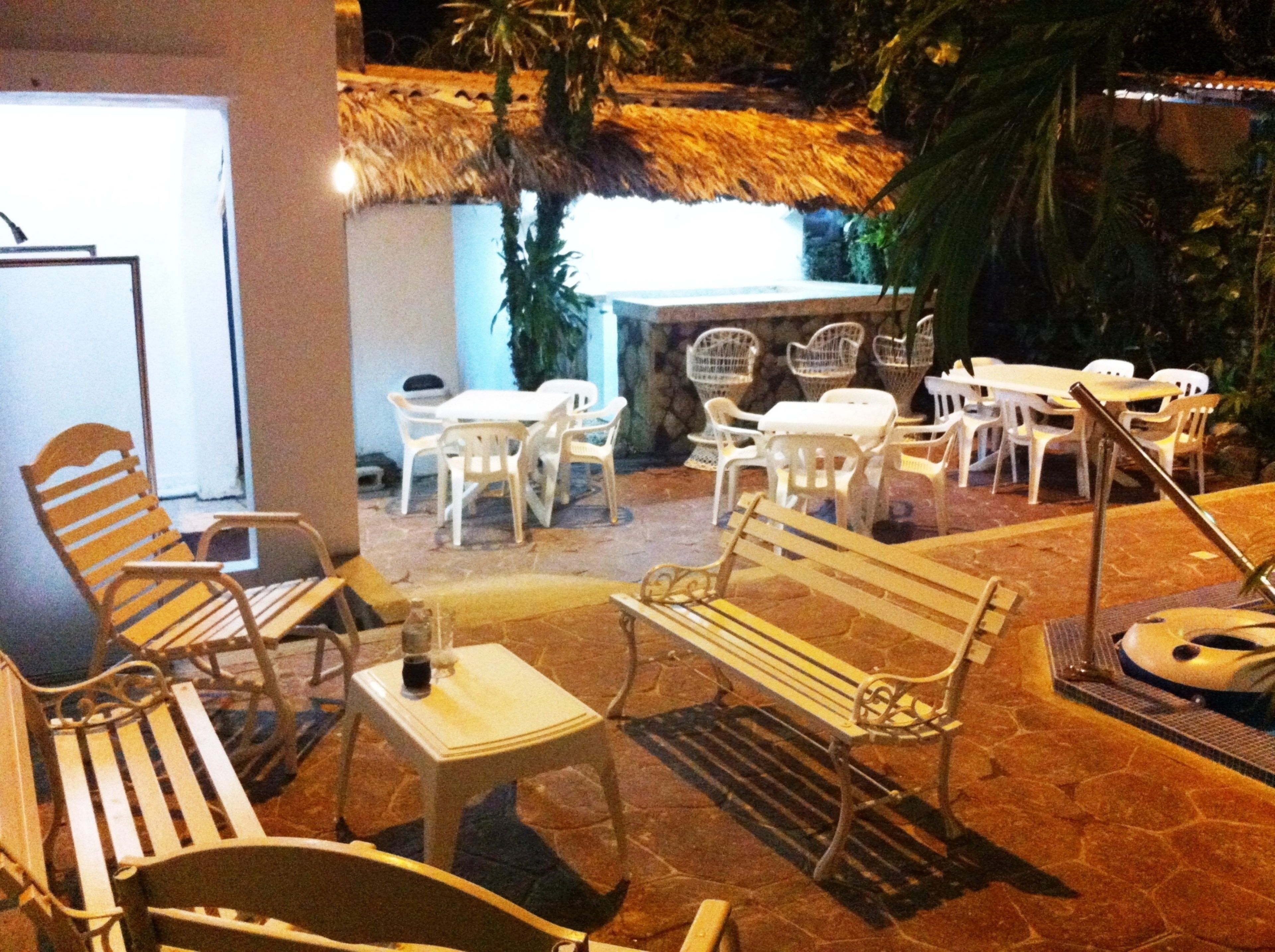 An outdoor seating area with wicker chairs and tables, a thatched roof, and a stone floor.