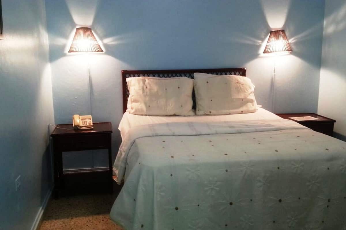 A bedroom with a bed, two bedside lamps, and a nightstand with a phone.