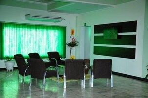 Zona de recepción con ventanal iluminado en verde, mostrador y varias sillas dispuestas para los huéspedes.
