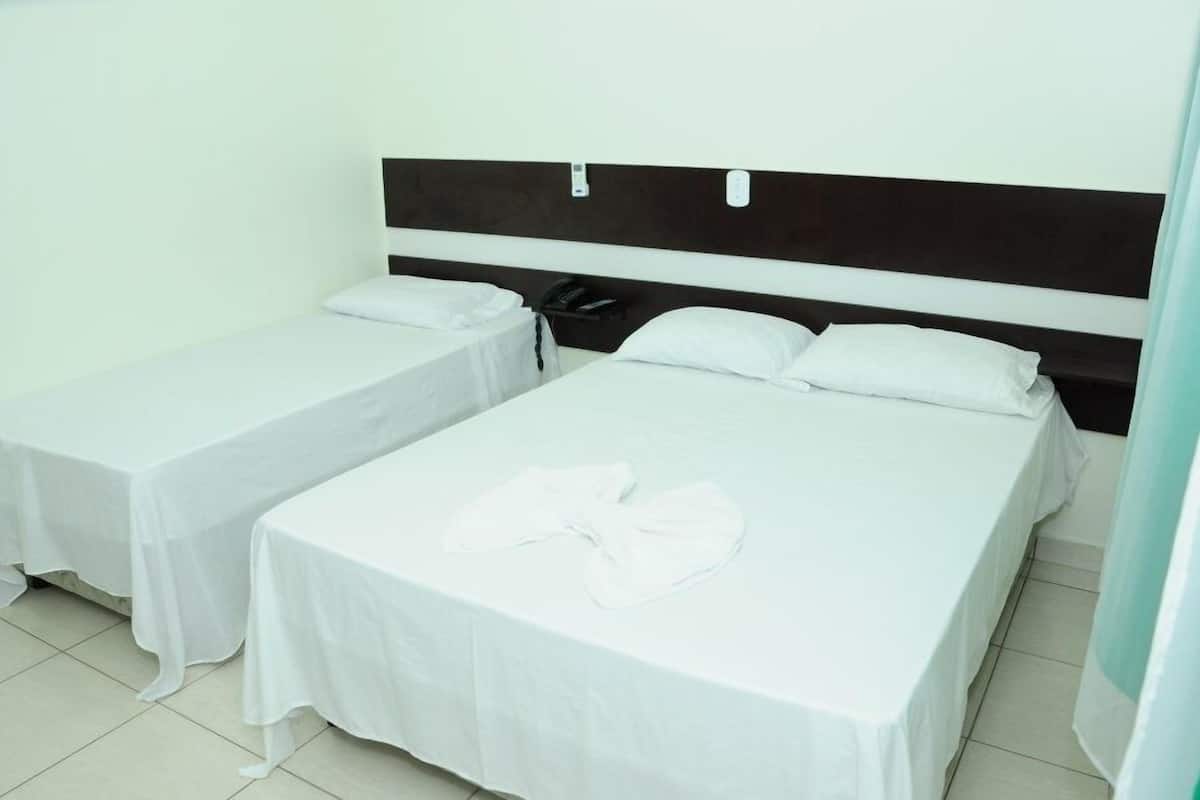 A hotel room with two single beds, each with a white bedspread and pillows, a bedside table with a phone, and a headboard with a control panel.