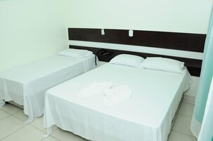 Habitación de hotel con dos camas individuales, cada una con colcha y almohadas blancas, una mesita de noche con teléfono y un cabecero con panel de control.