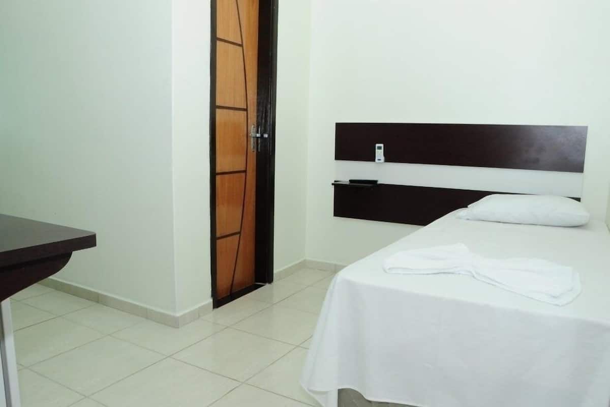 A hotel room with a bed, a bedside table, a wooden door, and a wall-mounted control panel.