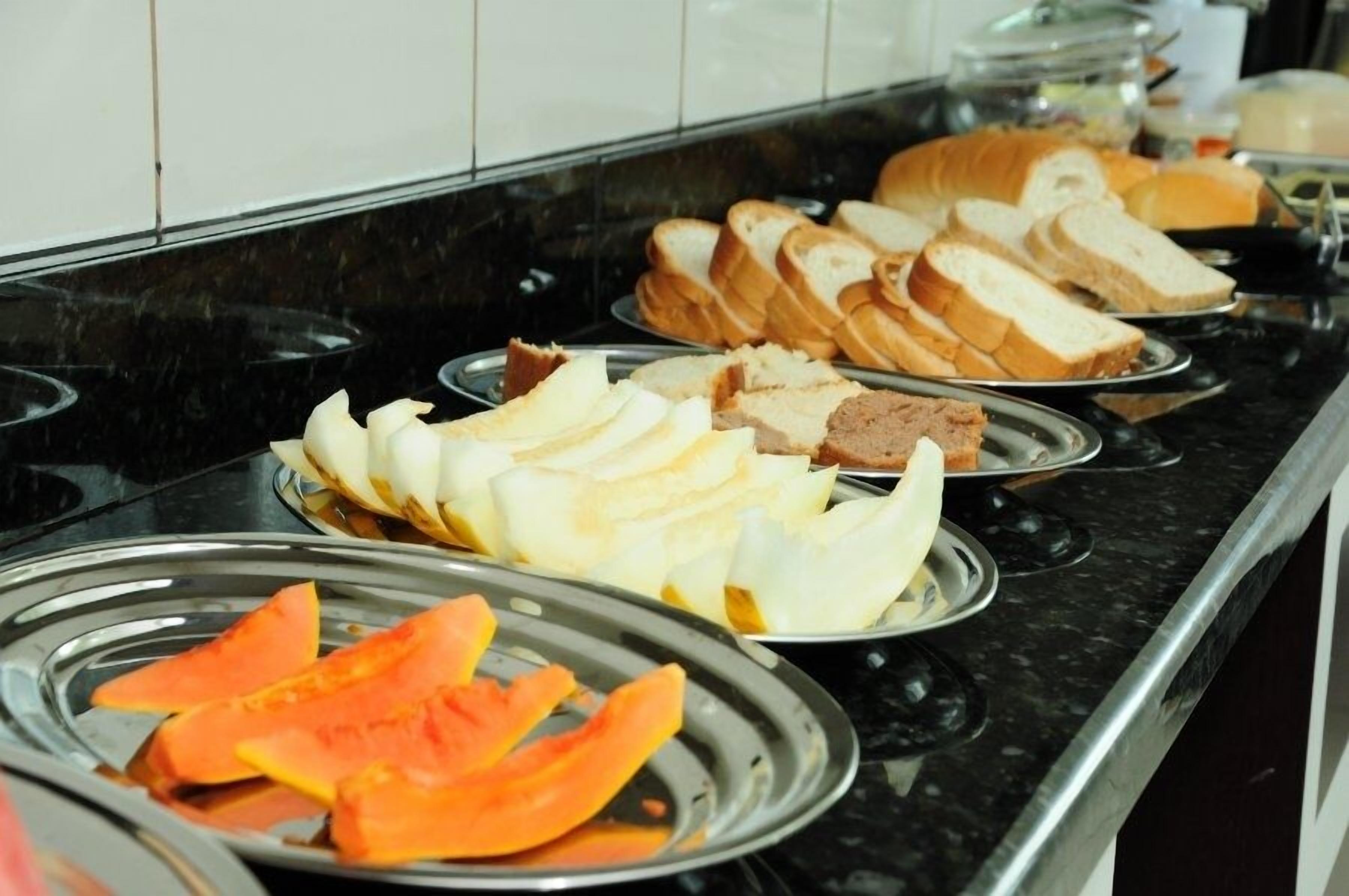 Un bufé con pan en rodajas, queso y frutas sobre bandejas de metal.