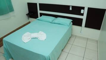 A single bed with a teal bedspread and white pillows, a black headboard, a bedside phone, and a white towel folded on the bed.