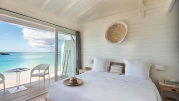 A bedroom with a large bed, a view of the sea, a balcony with chairs, and a woven wall hanging.