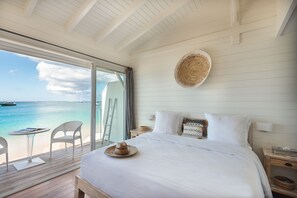 A bedroom with a large bed, a view of the sea, a balcony with chairs, and a woven wall hanging. - Le Temps des Cerises Hotel Beach (Grand Case)