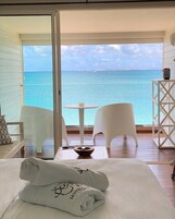 Un balcón con vistas al mar, una cama con toallas y dos sillones blancos de mimbre.