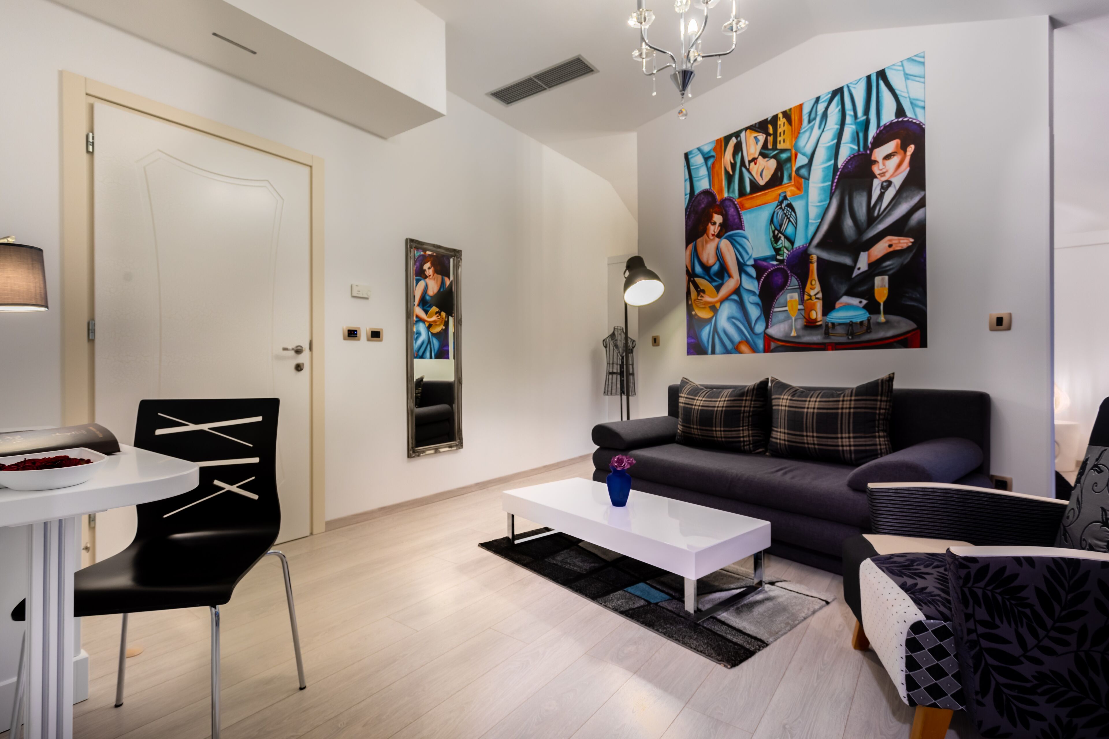 A modern living room with a white sofa, black and white armchairs, a white coffee table, and a painting on the wall.