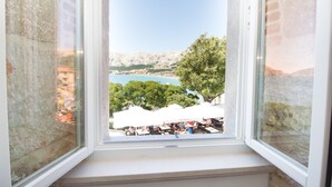 A view from a window overlooking a coastal area with outdoor seating and a mountain backdrop. - Heritage hotel Forza (Baska)