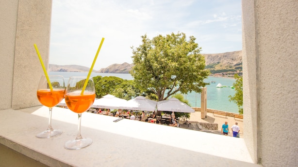 Two glasses of orange beverage on a ledge with a view of a lake and mountains in the background. - Heritage hotel Forza (Baska)