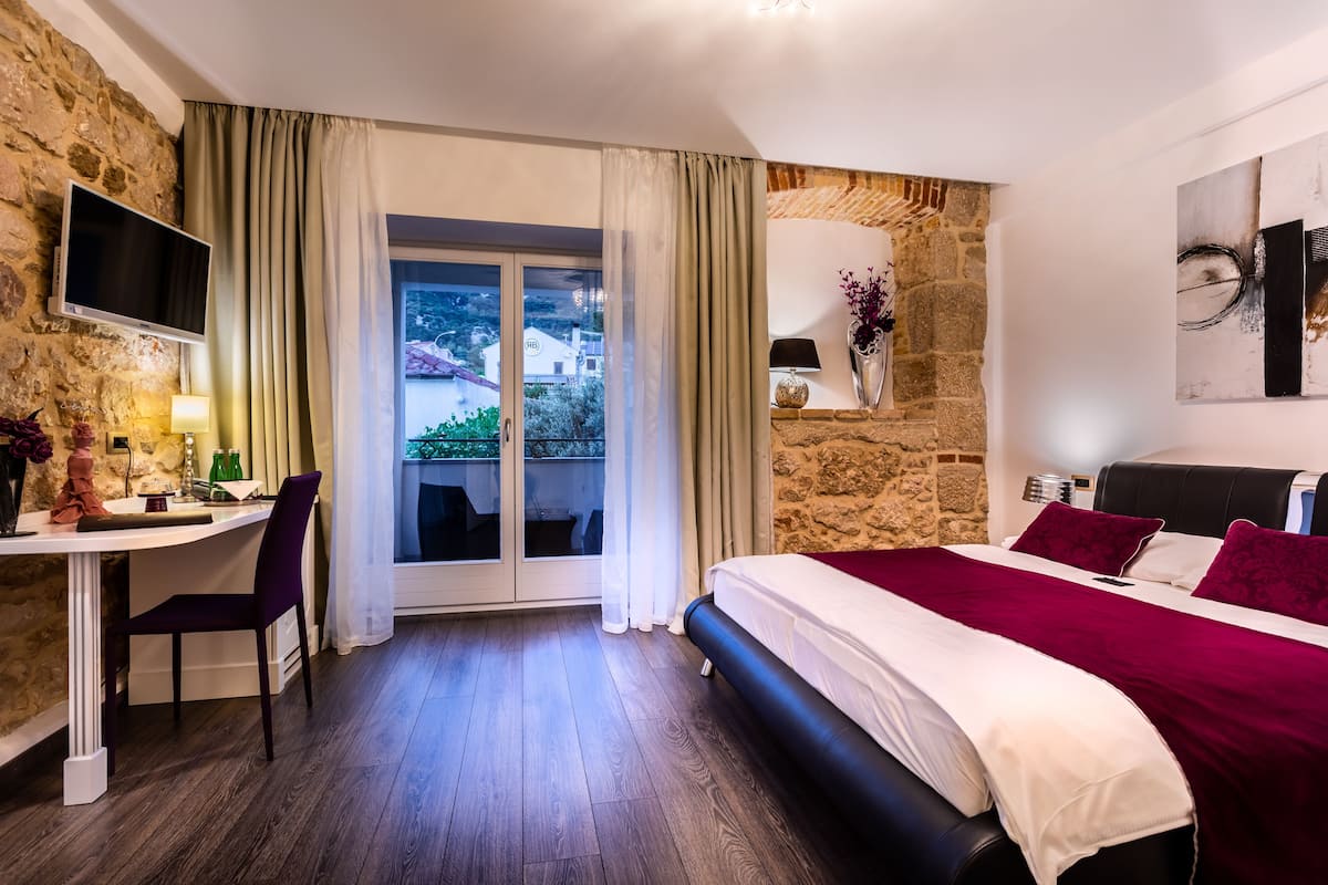 A bedroom with a bed, a desk, a chair, a TV, and a view of the outside.