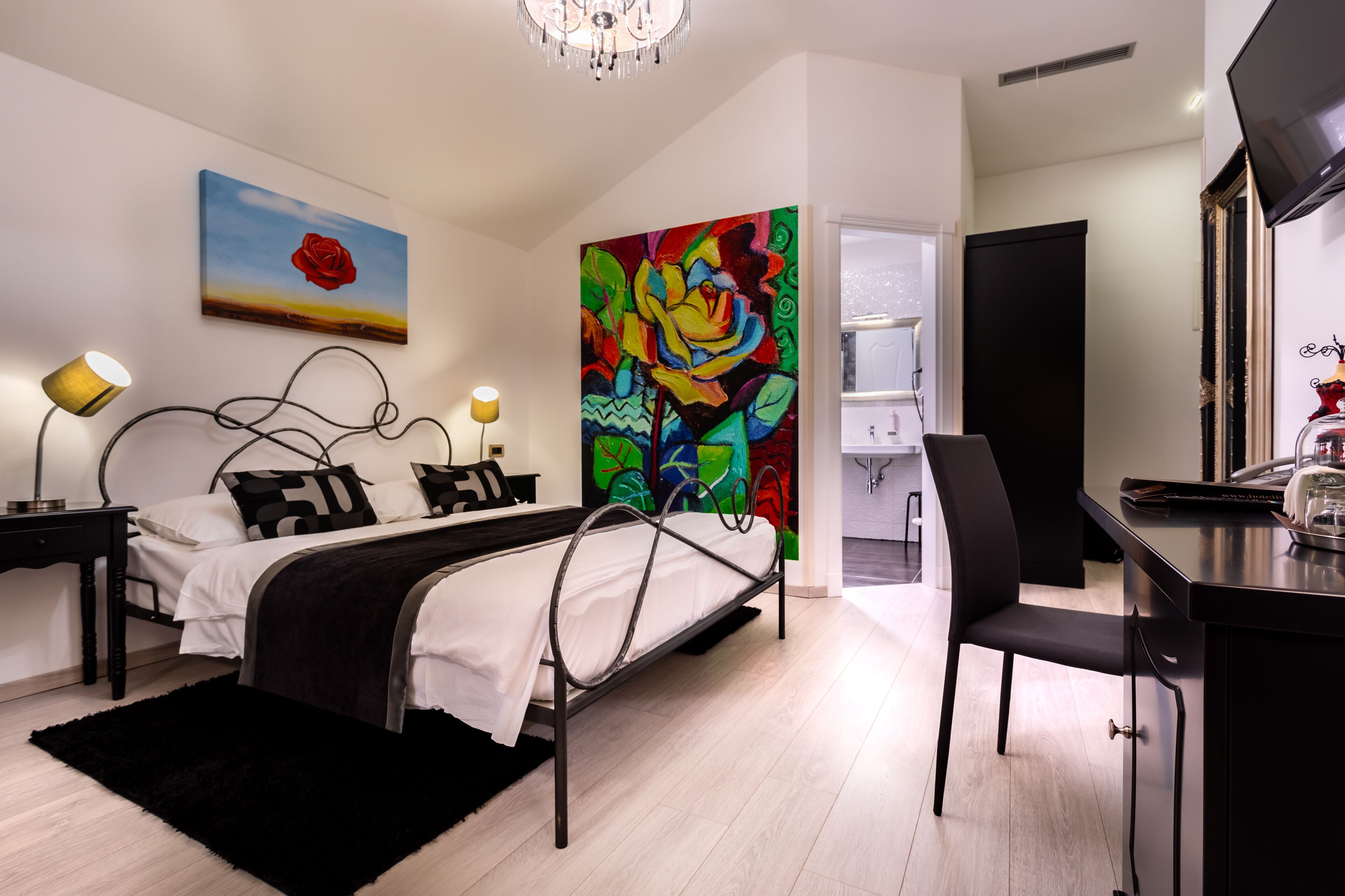 A modern bedroom with a bed, bedside lamps, a desk, and a large colorful painting.