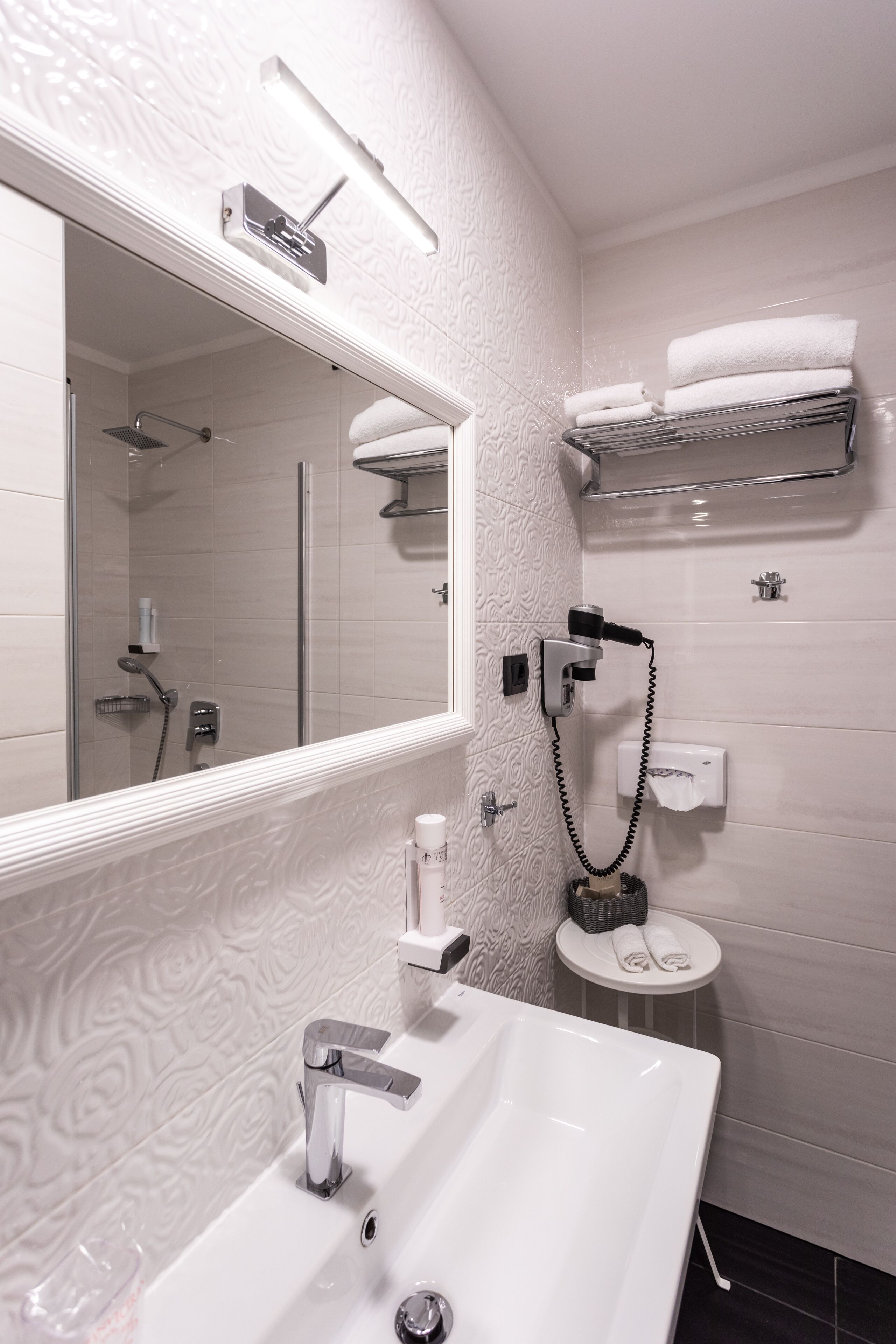 Une salle de bain moderne avec un grand miroir, un lavabo blanc, une douchette à main et un porte-serviettes.