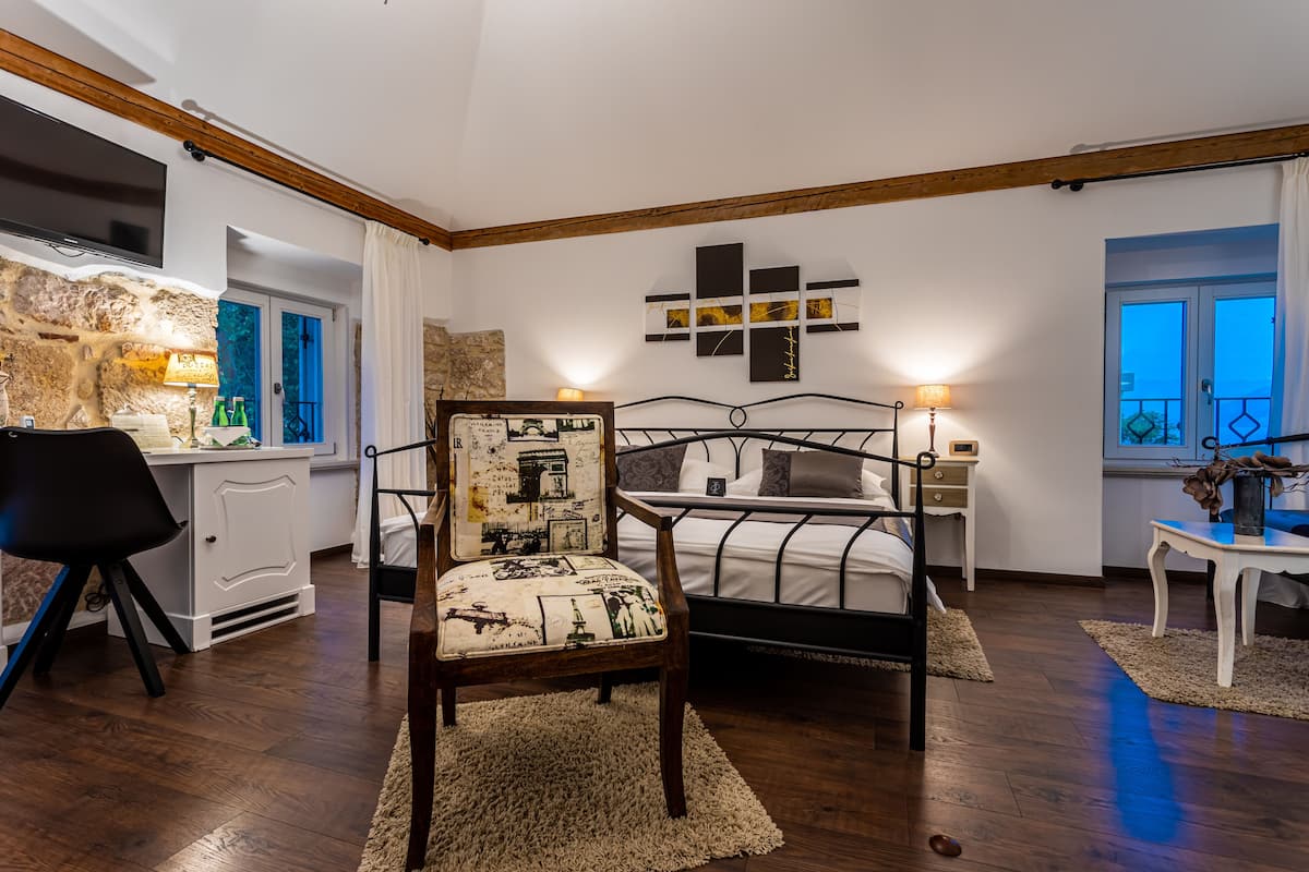A bedroom with a bed, a chair, a desk, a TV, and a window.