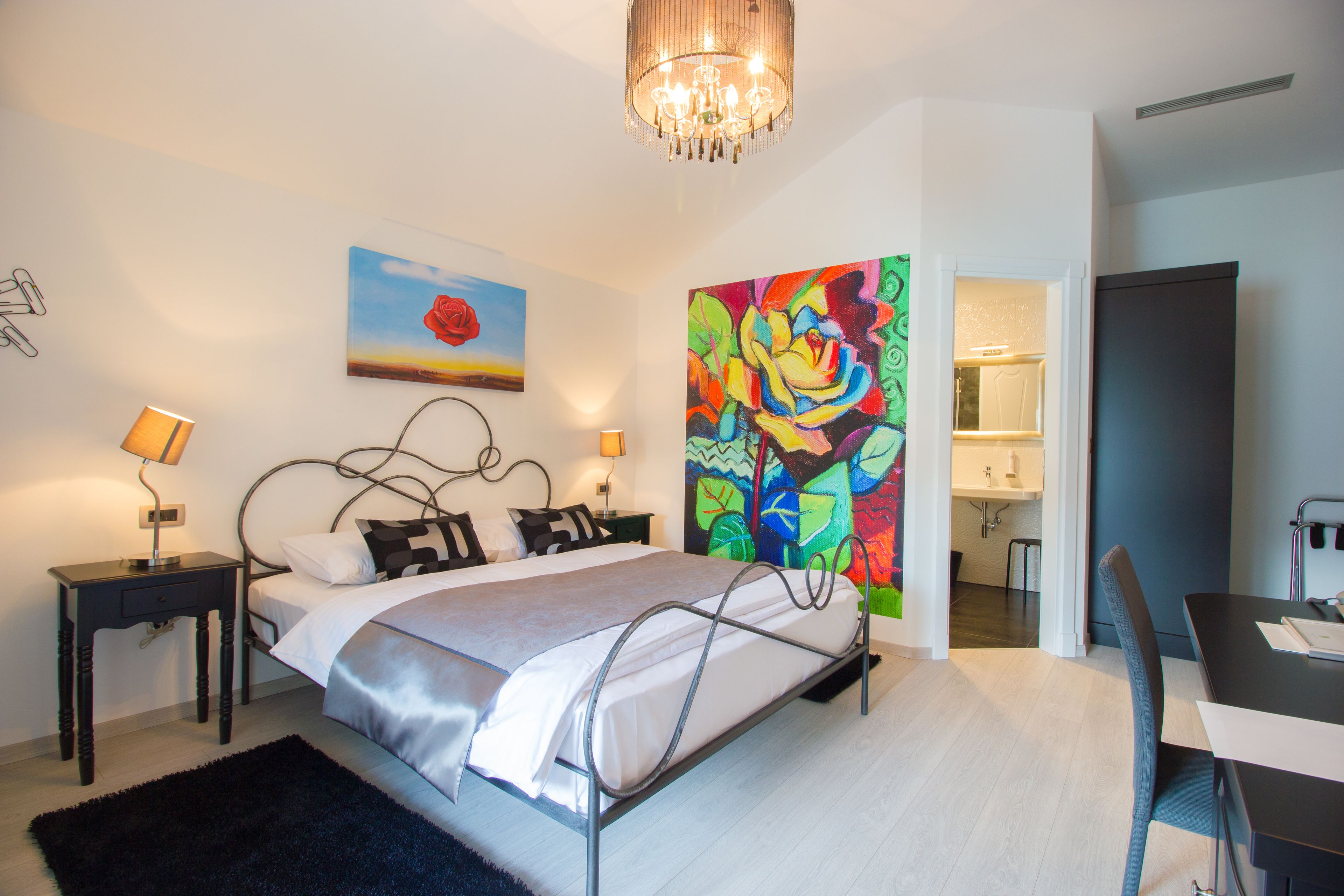 A modern bedroom with a bed, bedside tables, a desk, and a colorful abstract painting.