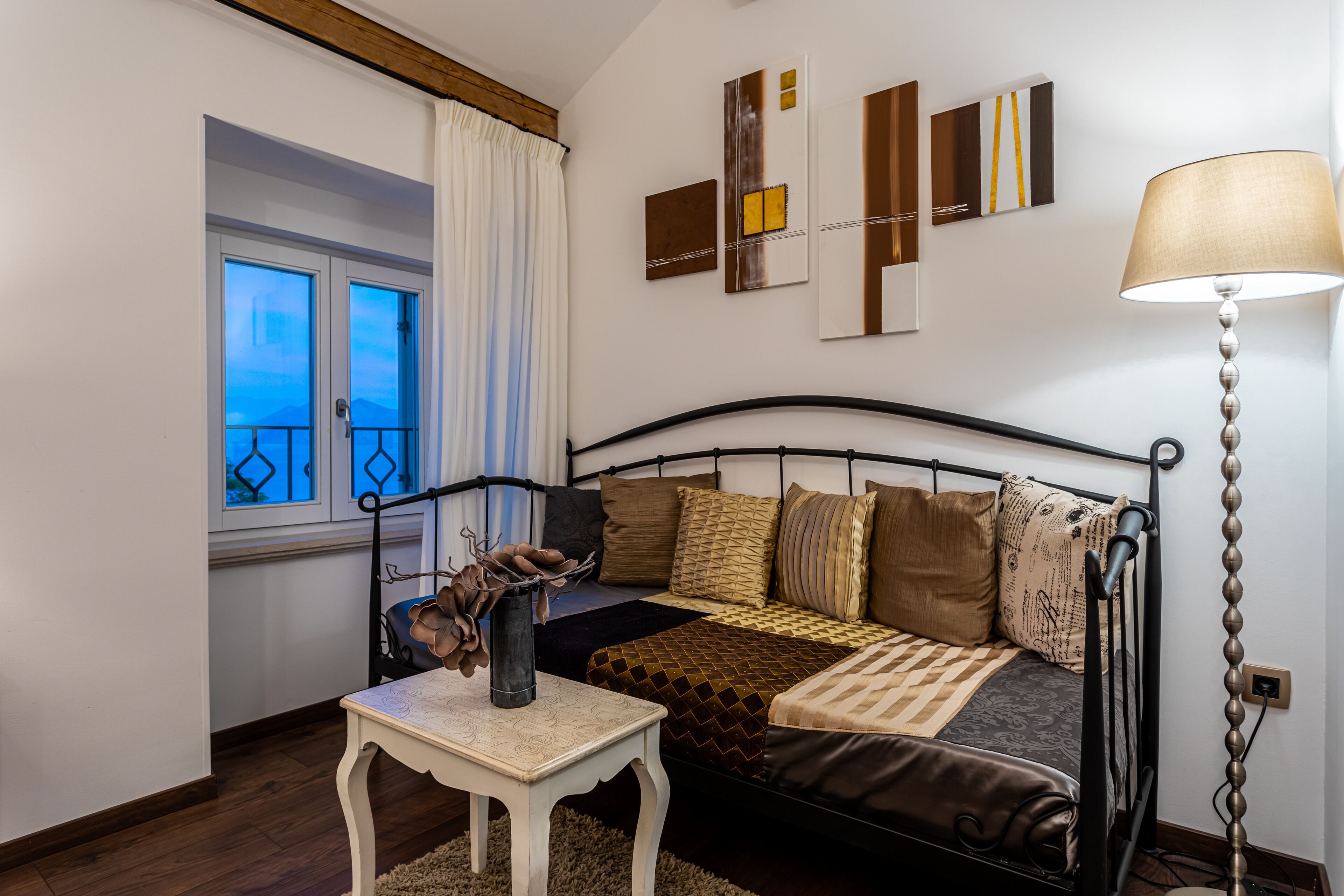 A bedroom with a bed, a bedside table, a lamp, a window with curtains, and wall art.