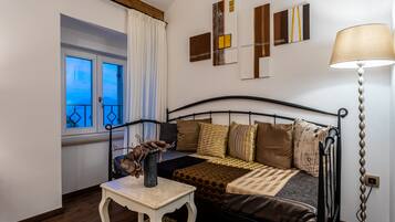 A bedroom with a bed, a bedside table, a lamp, a window with curtains, and wall art.