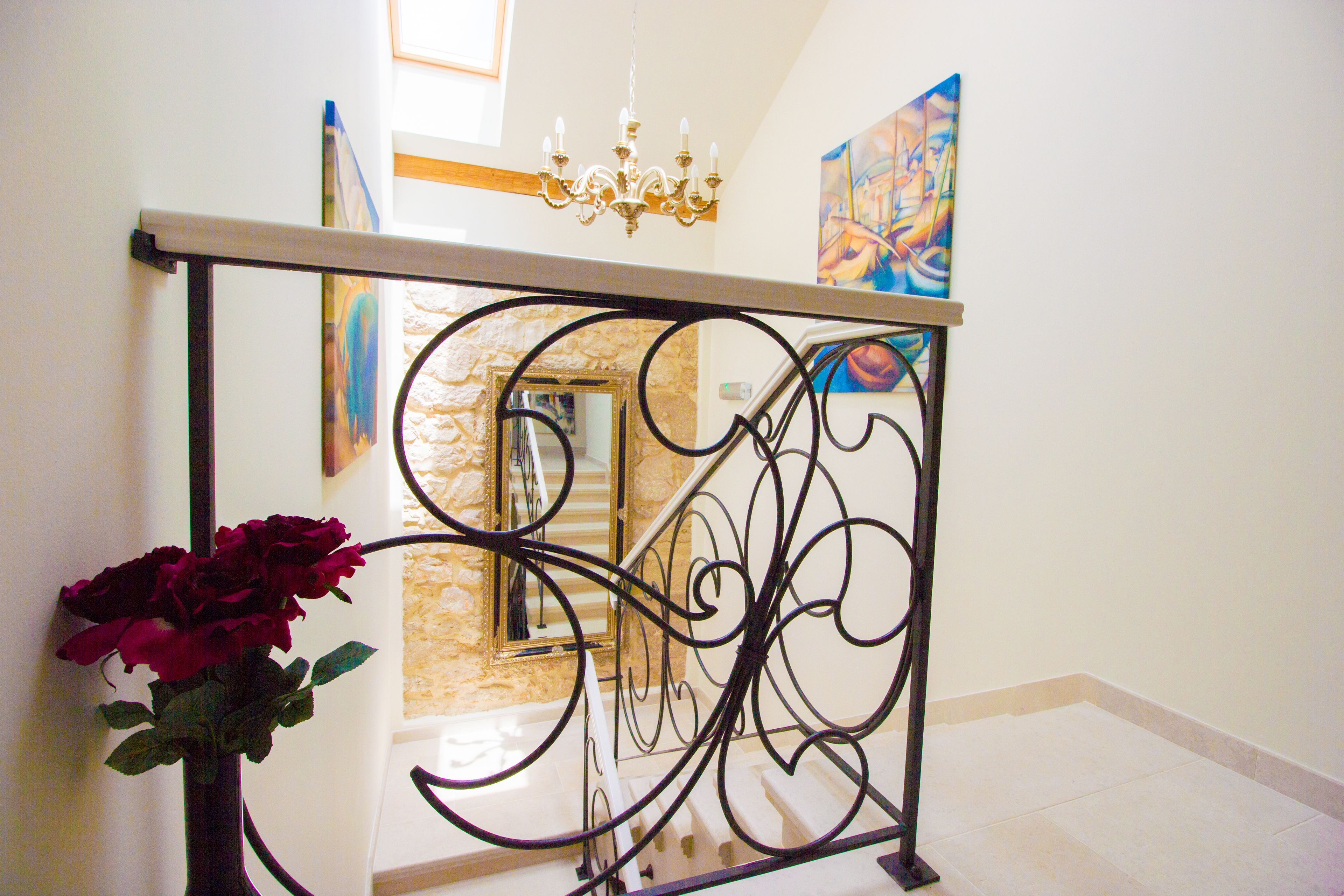 Una escalera con barandilla de hierro forjado, un candelabro y un jarrón con rosas rojas.