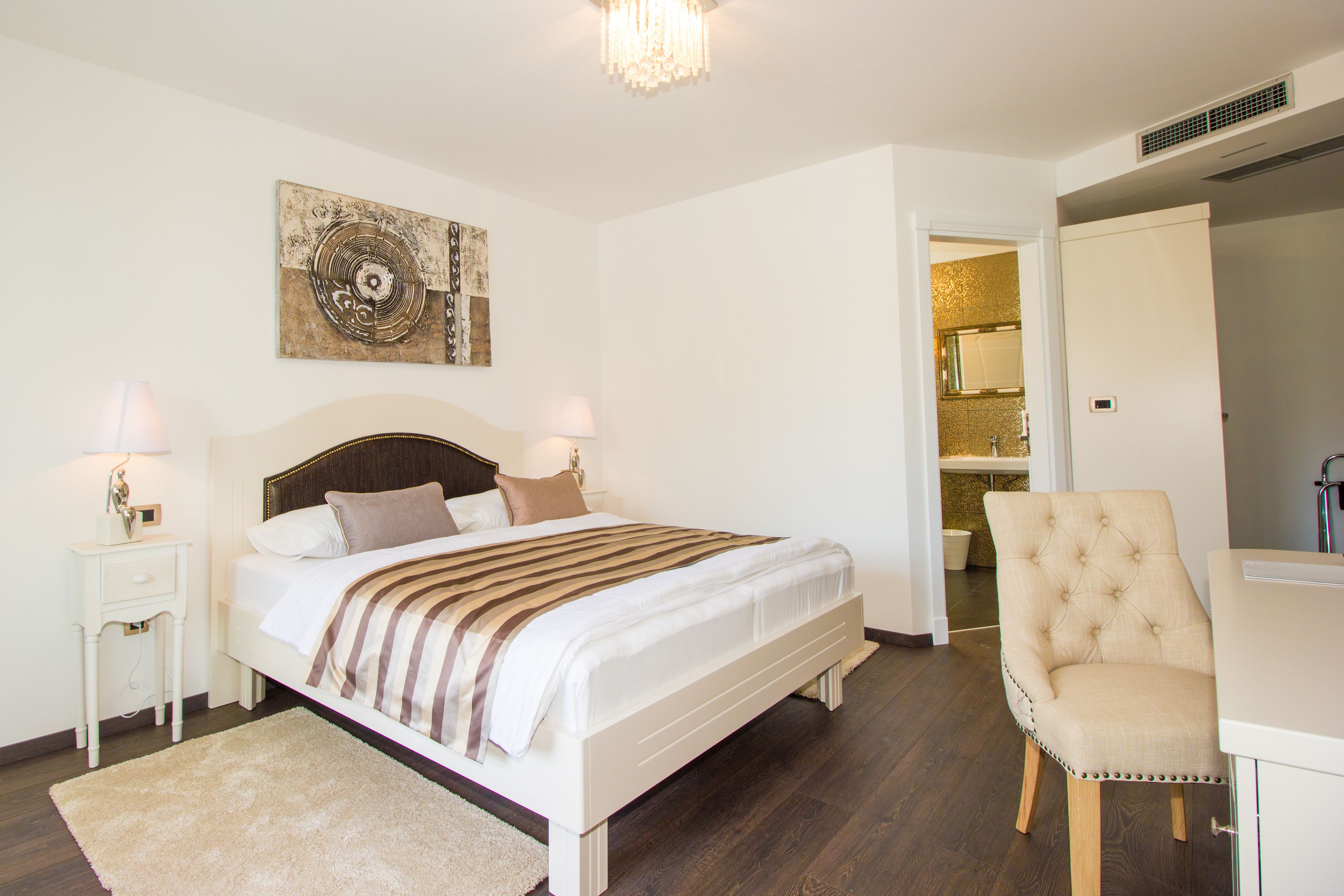 Une chambre à coucher avec un lit, des tables de chevet, une chaise et une salle de bain visible à travers une porte ouverte.