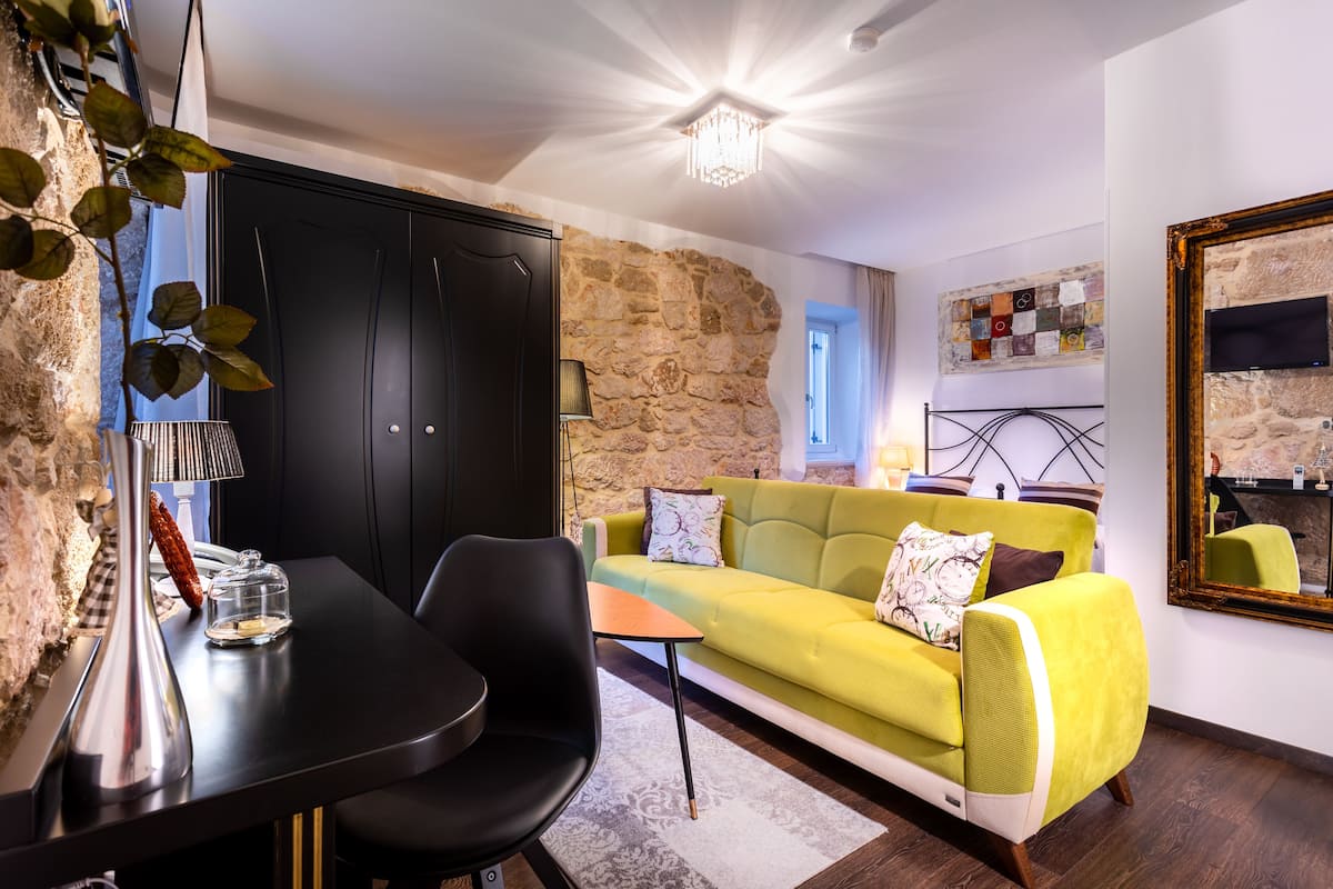 A modern living room with a stone wall, a yellow sofa, a black dining table, and a chandelier.