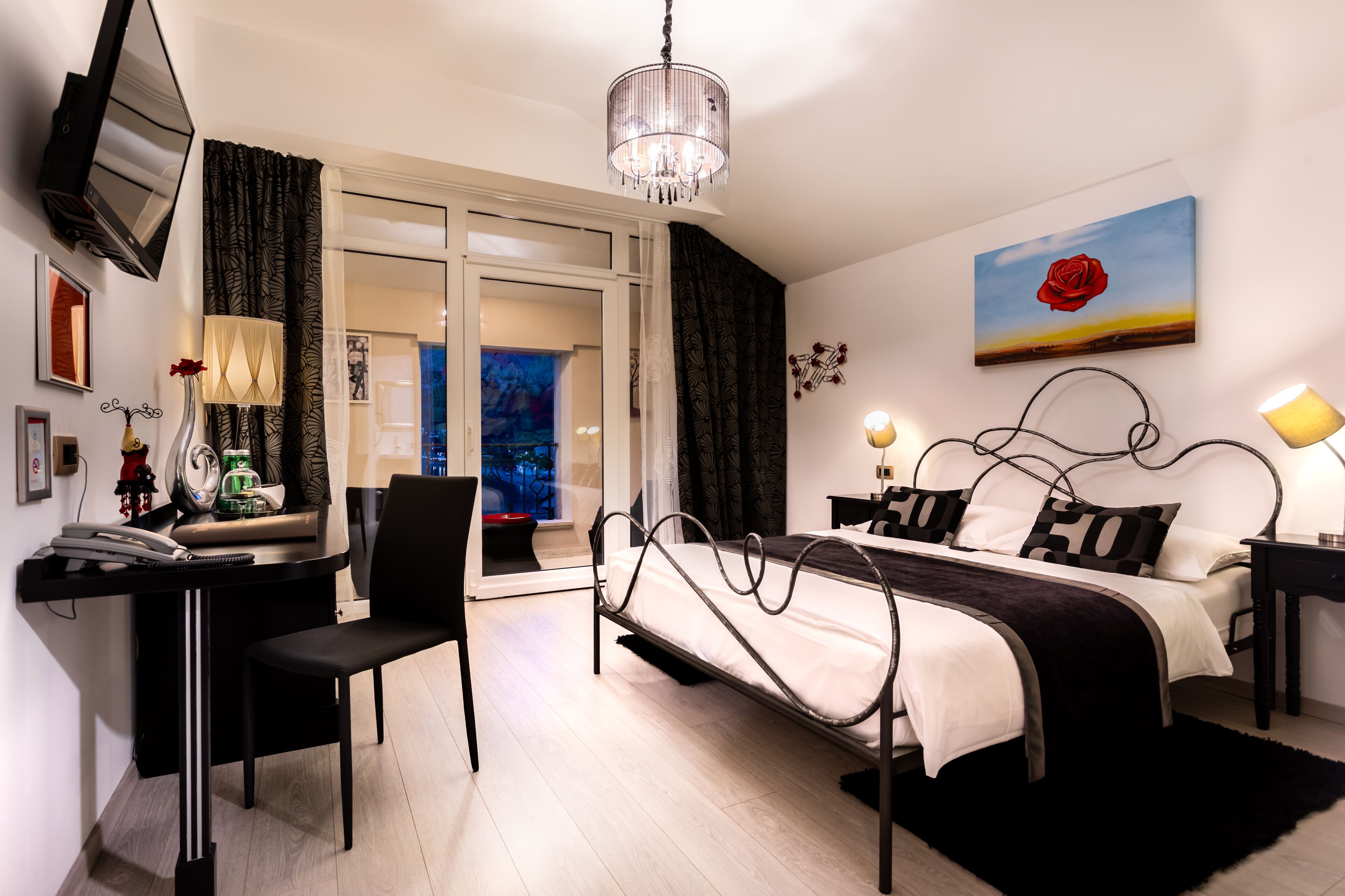 A modern bedroom with a bed, desk, chair, and a painting of a rose.