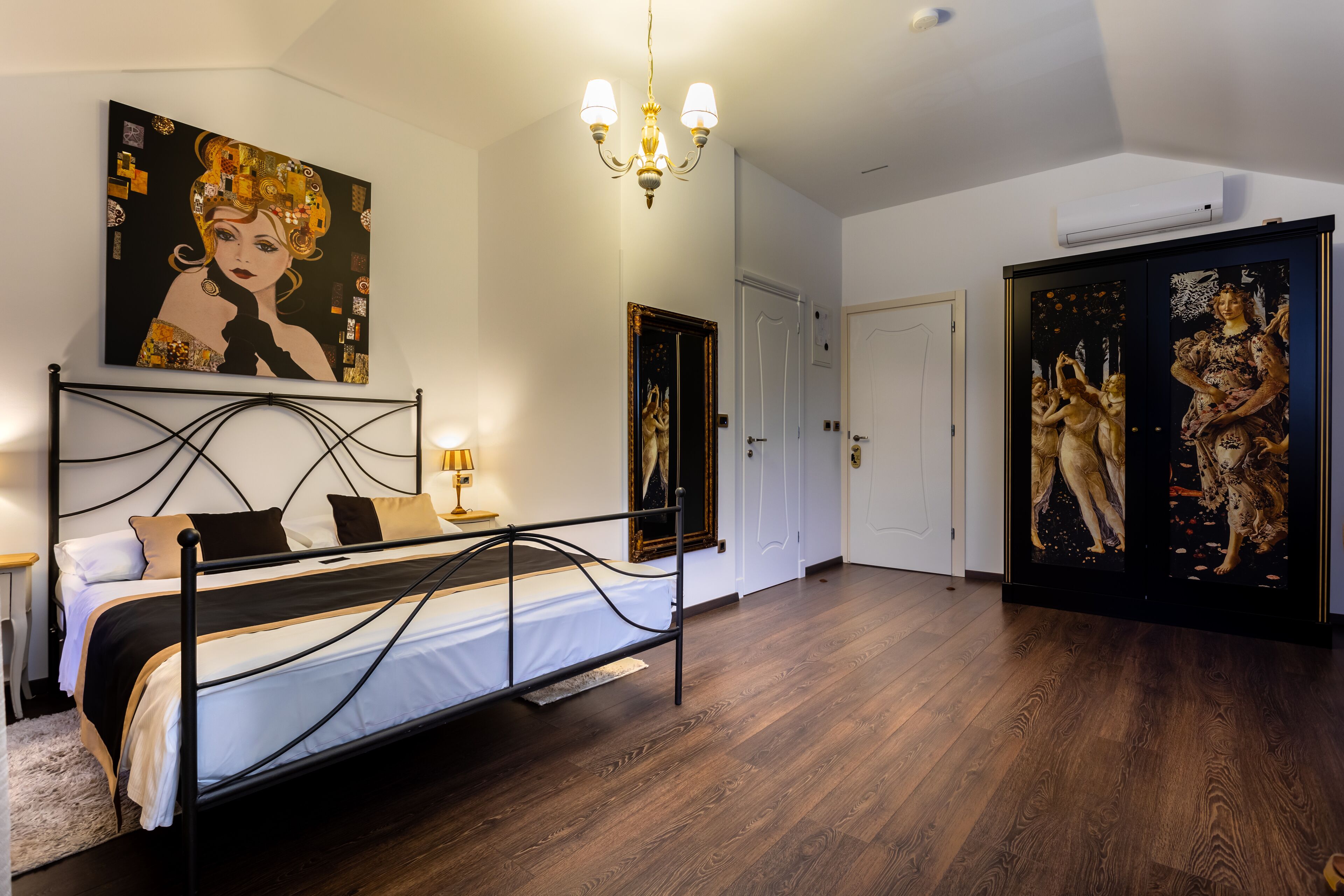 A bedroom with a bed, a chandelier, and artwork on the walls.